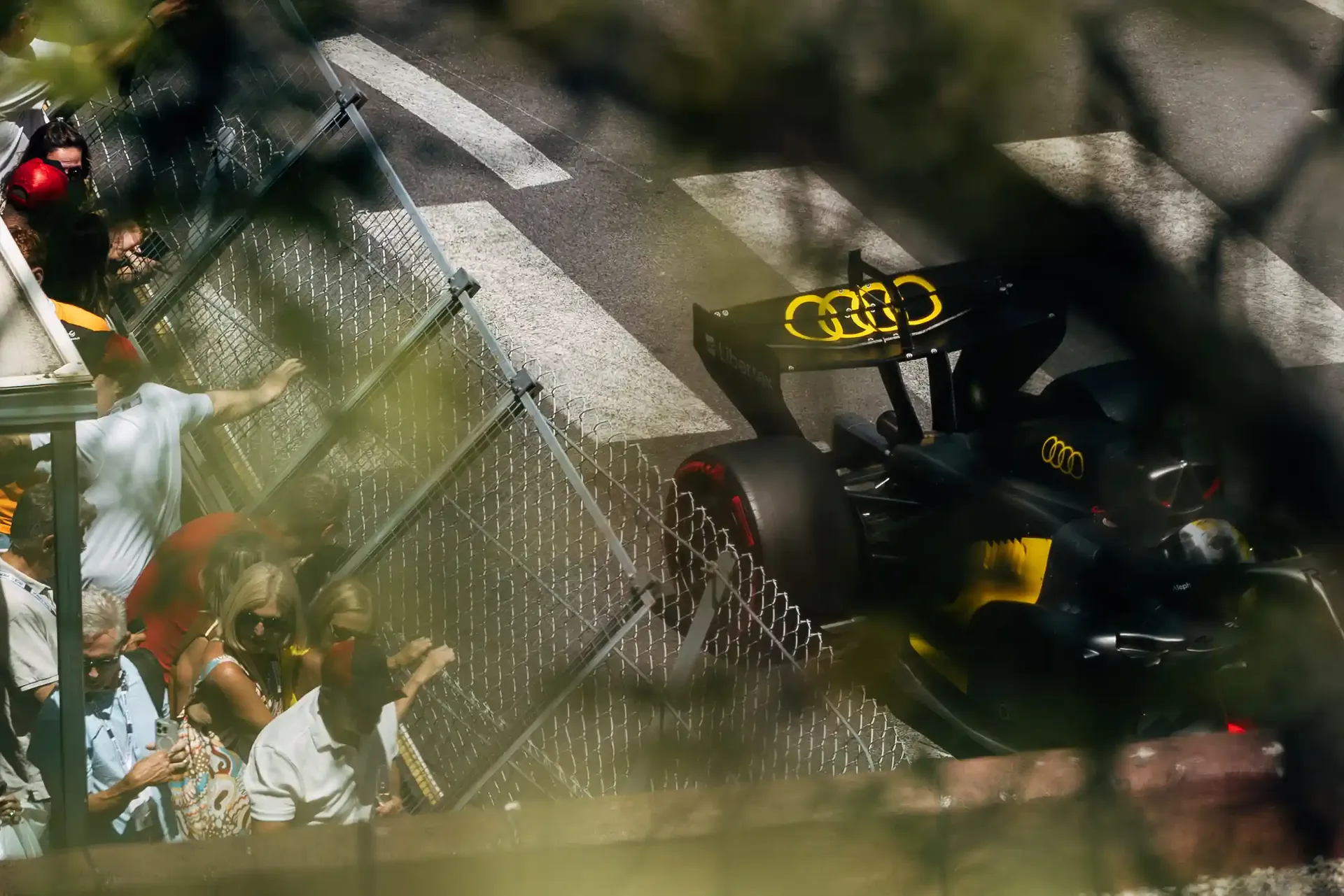 Audi Revolut F1® car R26 captured through fencing and foliage while navigating the Monaco street circuit.