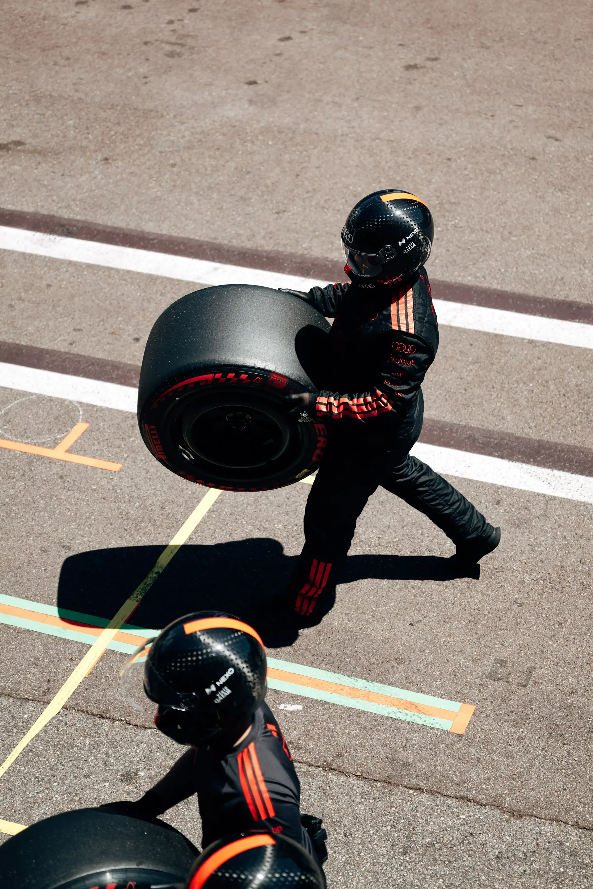 Audi Revolut F1® Team mechanic carries a Pirelli tyre through the Monaco pit lane, viewed from above.