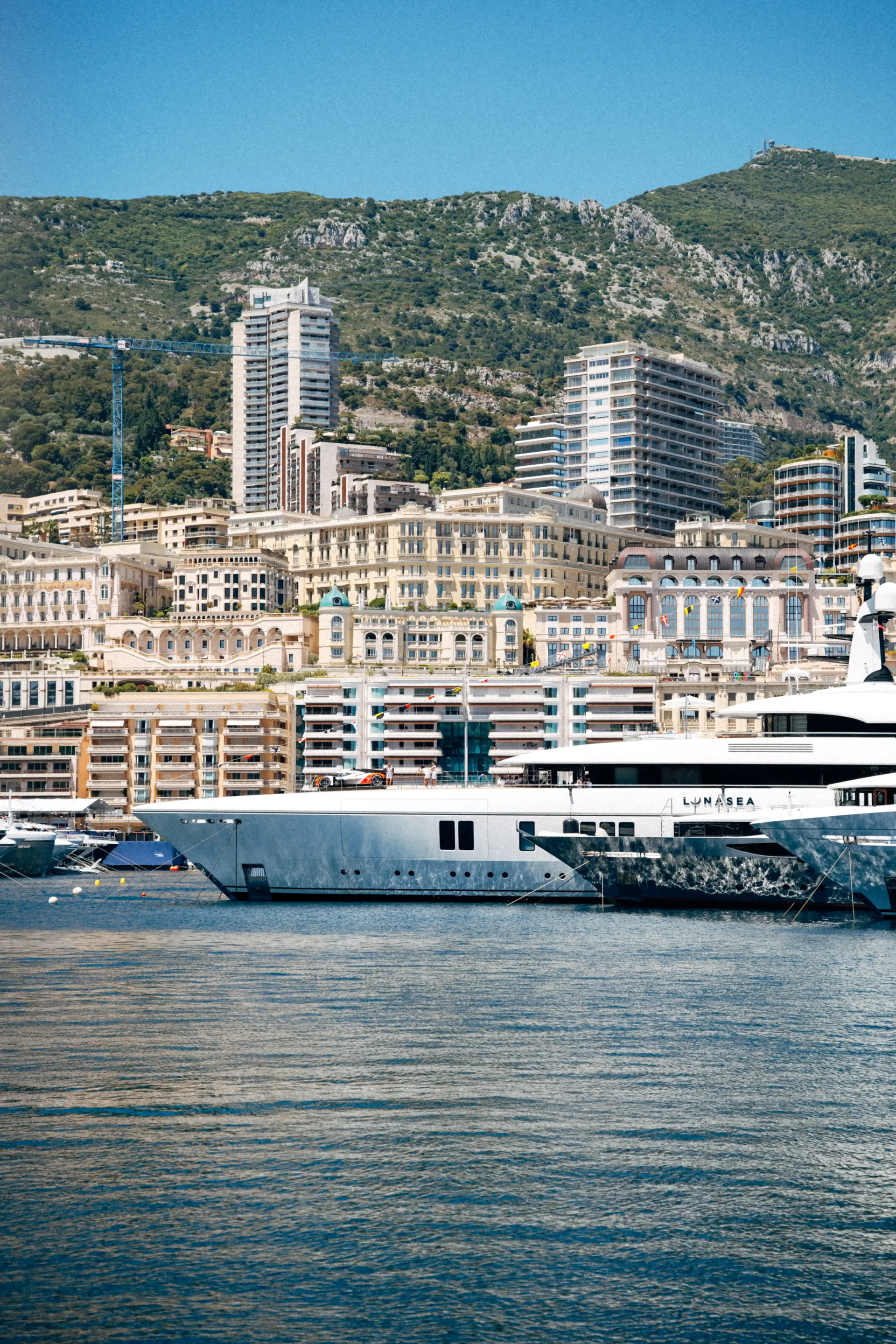 Panoramic view of Monaco harbor with luxury yachts, waterfront buildings, and hills in the background.