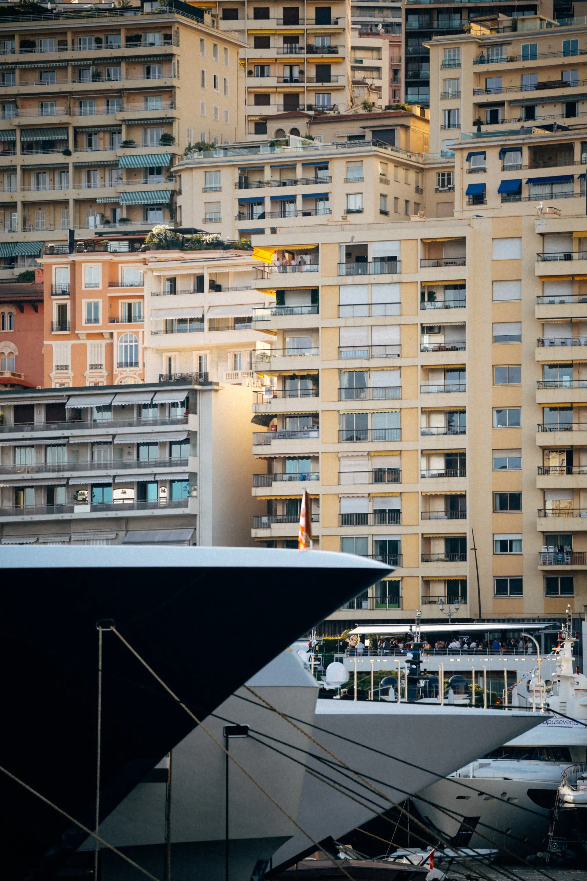 Dense Monaco apartment buildings rising above a marina with yacht masts in the foreground.