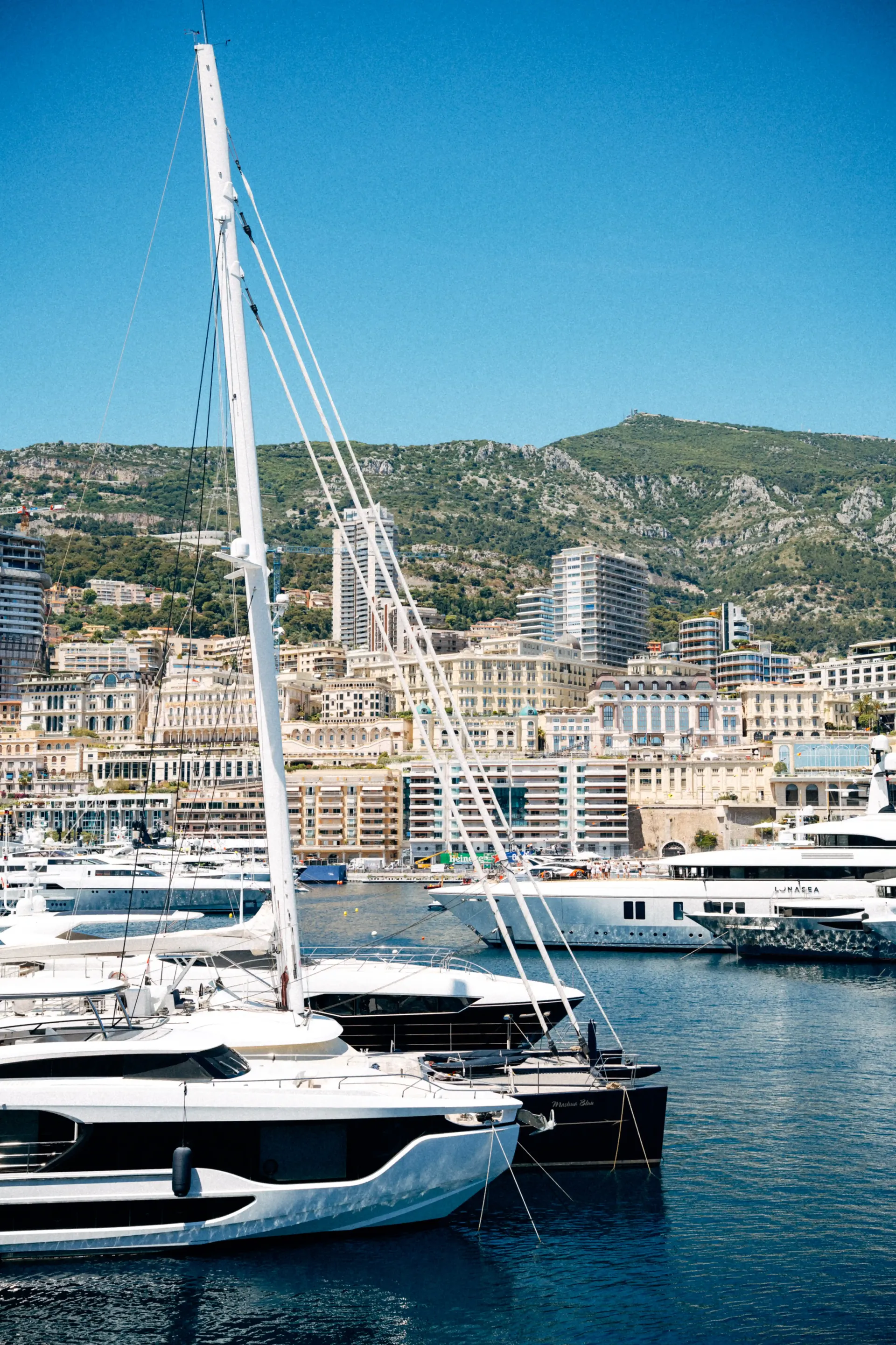 Sailboats and yachts in Monaco harbor with hillside buildings under clear blue skies.