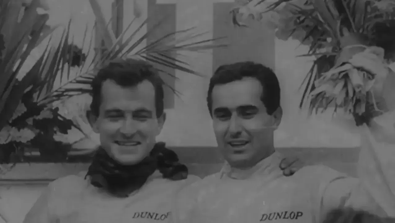 Black and white archive footage of two smiling drivers in Dunlop overalls with flowers