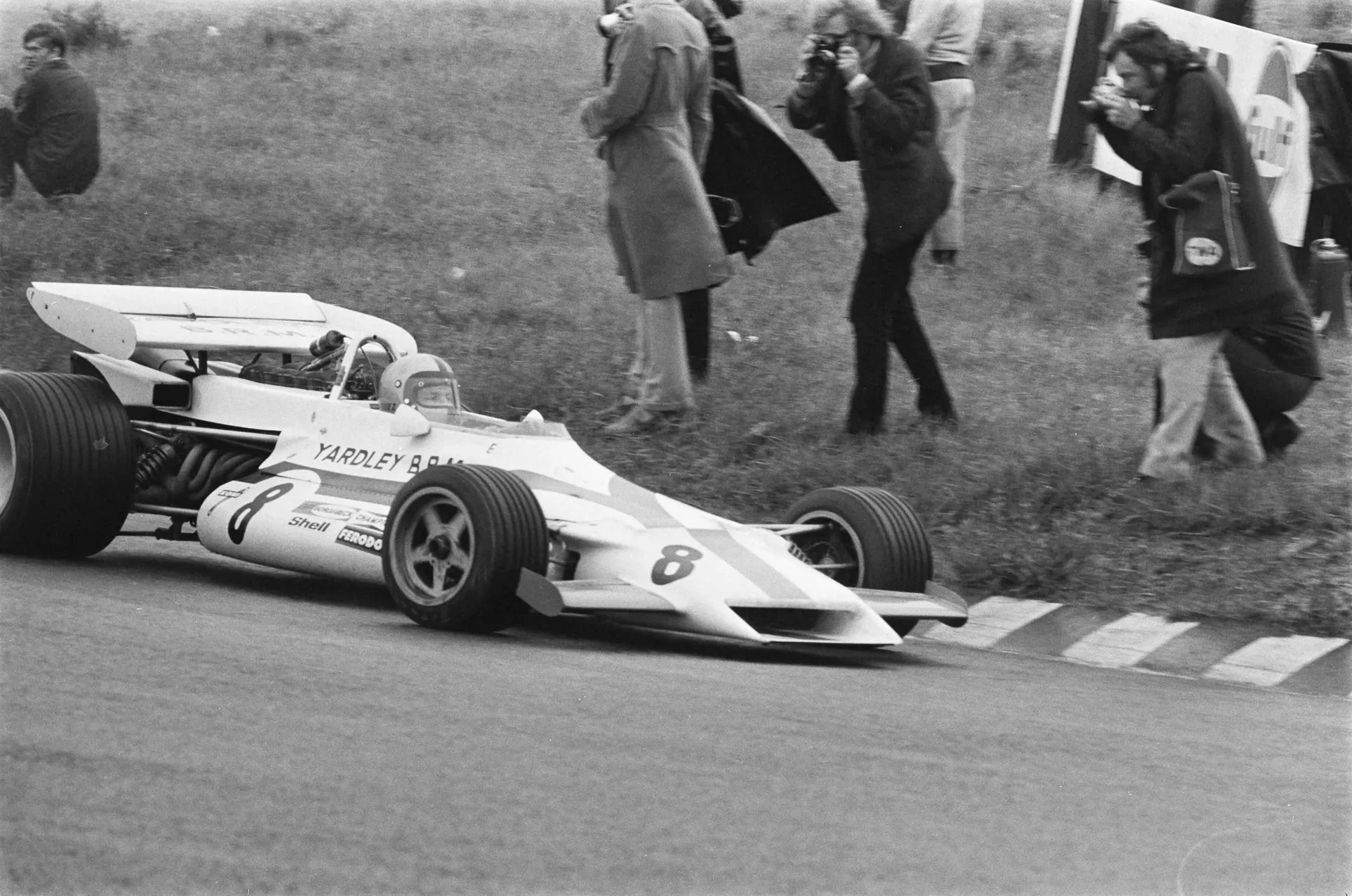 Black and white photo of the white Yardley BRM car number 8 cornering past photographers at the track