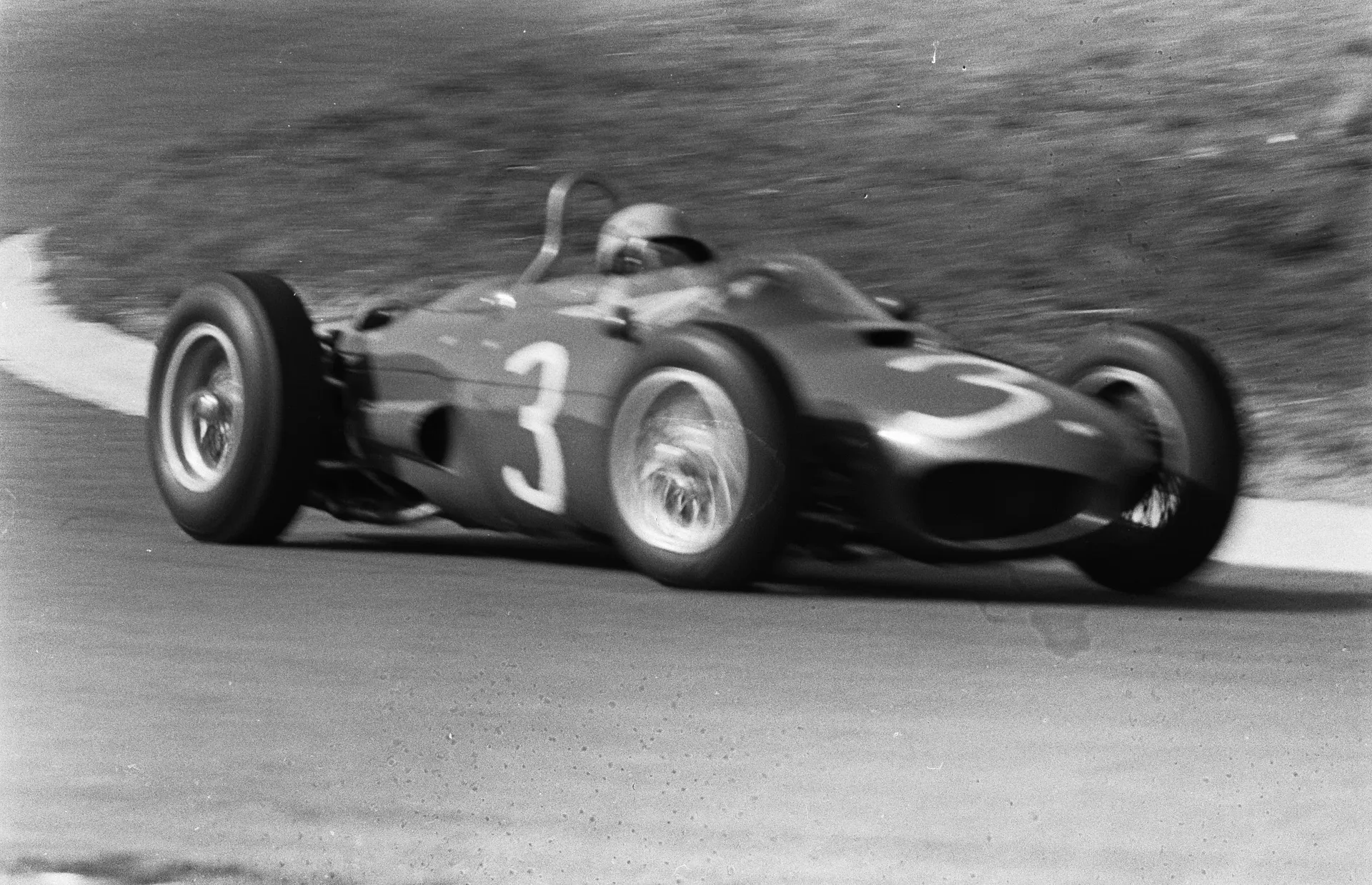 Black and white photo of a vintage race car with number 3 speeding through a corner, motion blurred