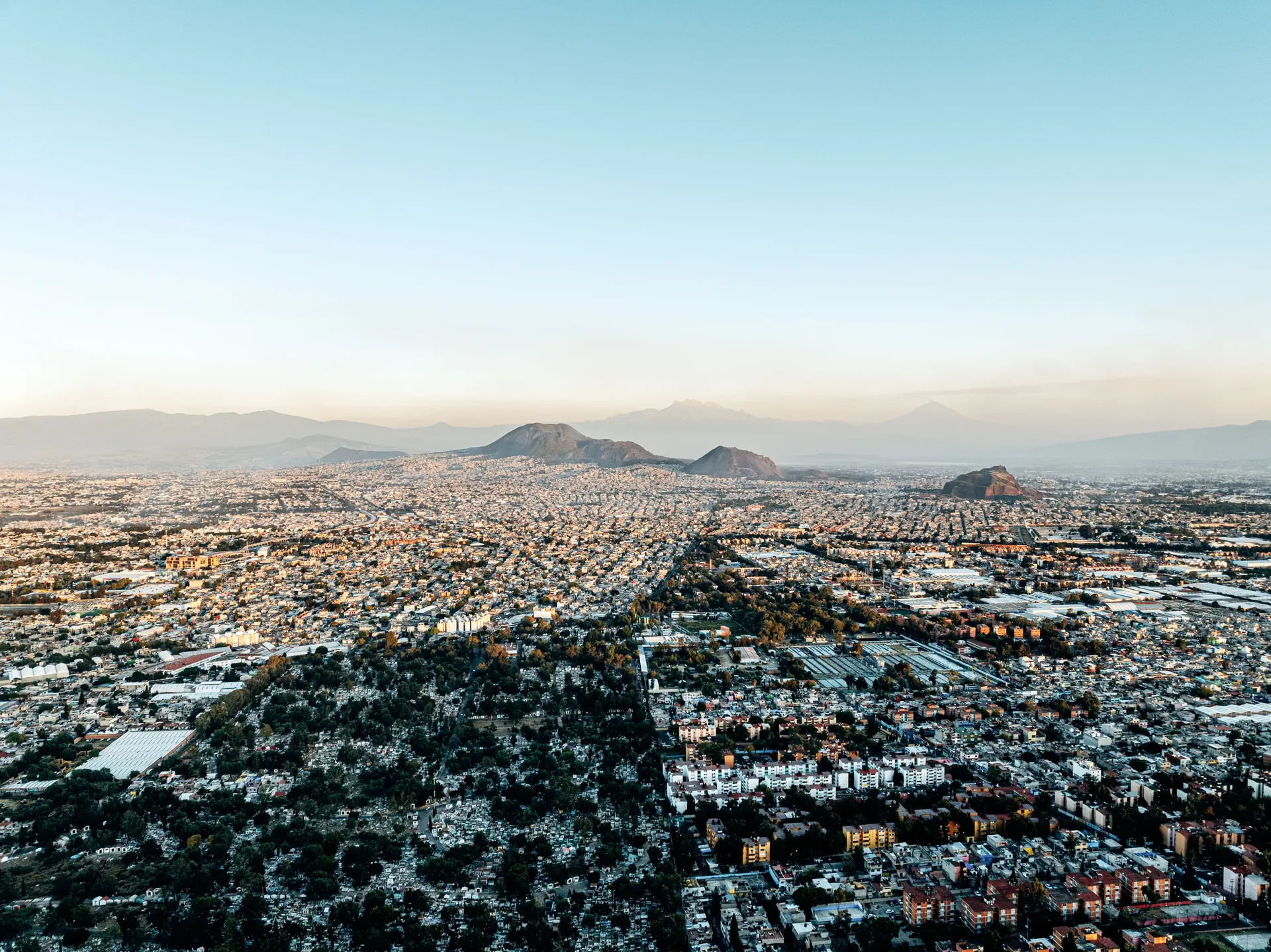Aerial view of Mexico City in golden light with volcanoes on the horizon
