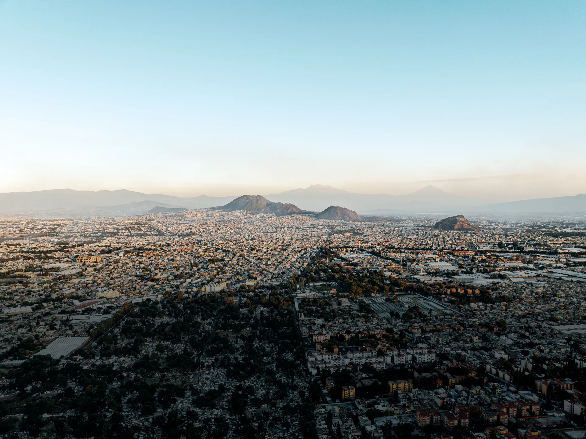 Aerial view of Mexico City in golden light with volcanoes on the horizon