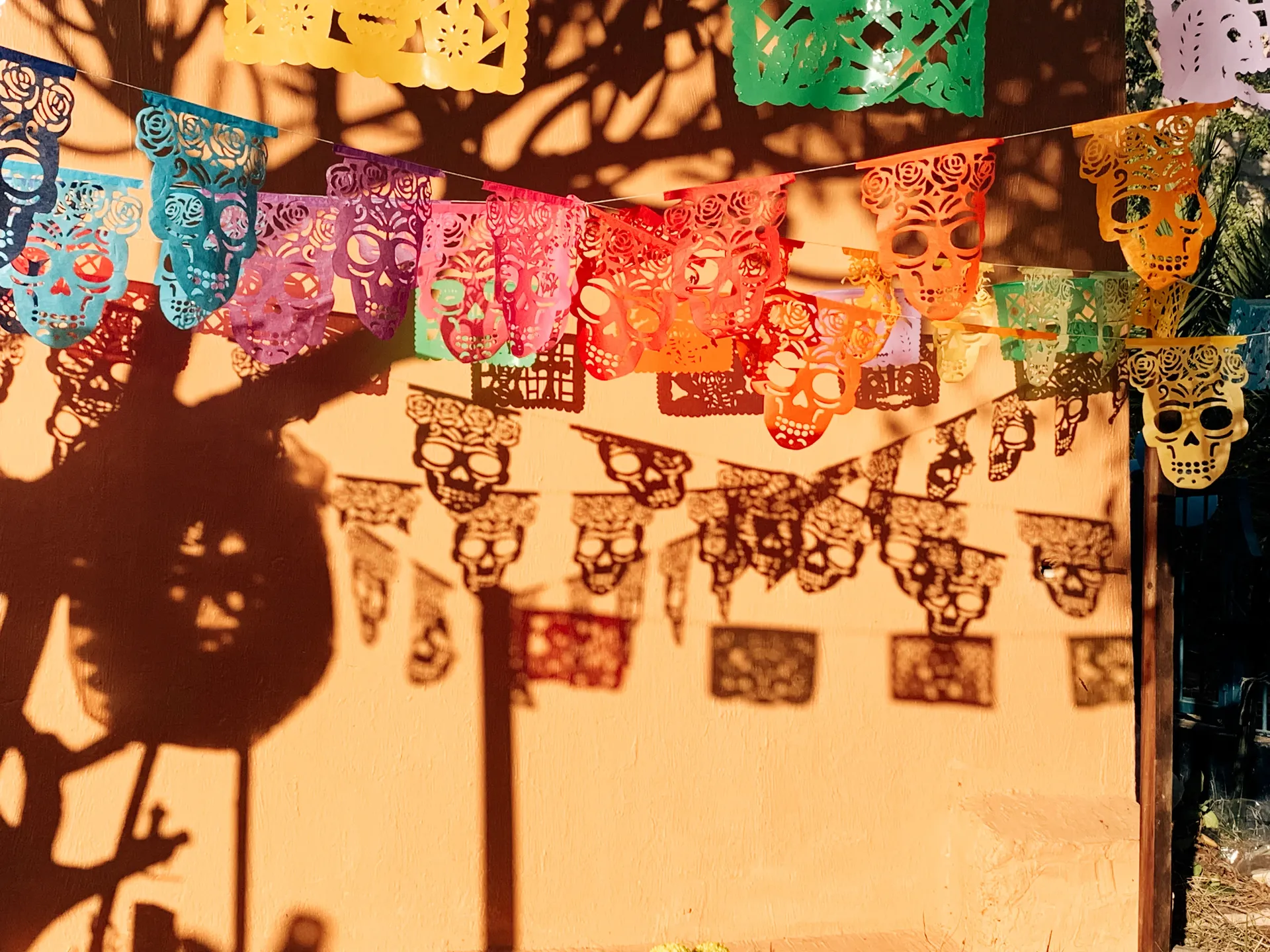 Colourful papel picado banners with cut-out skulls casting shadows on an orange wall