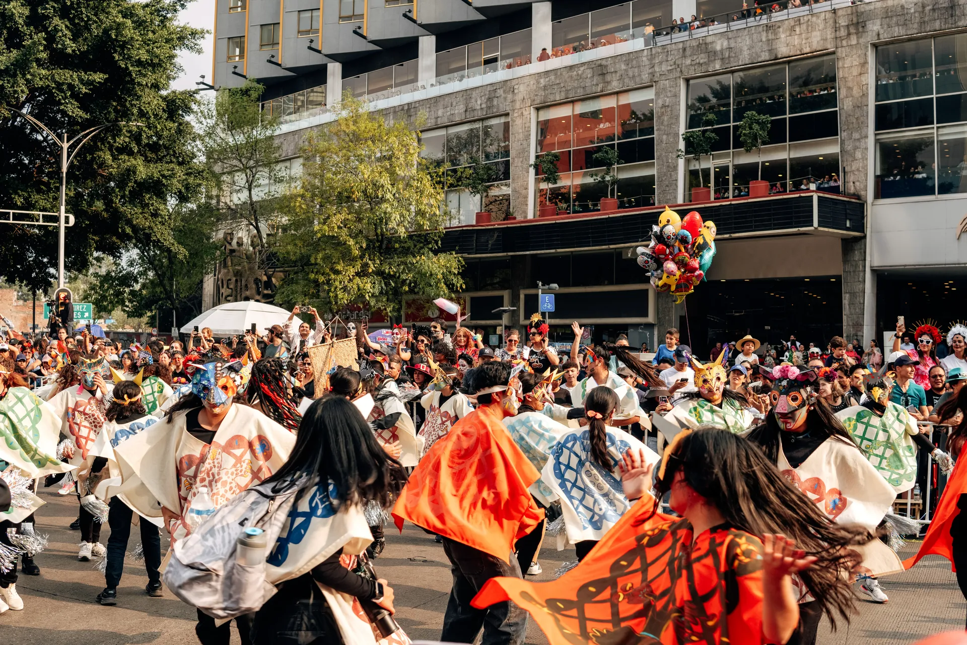 Masked dancers in painted ponchos at the Día de los Muertos parade in Mexico City, watched by crowds
