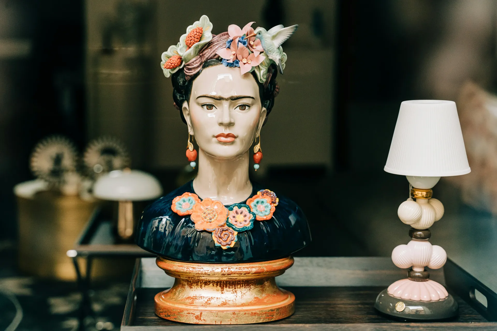 Porcelain bust of Frida Kahlo with a flower crown and hummingbird next to a small table lamp