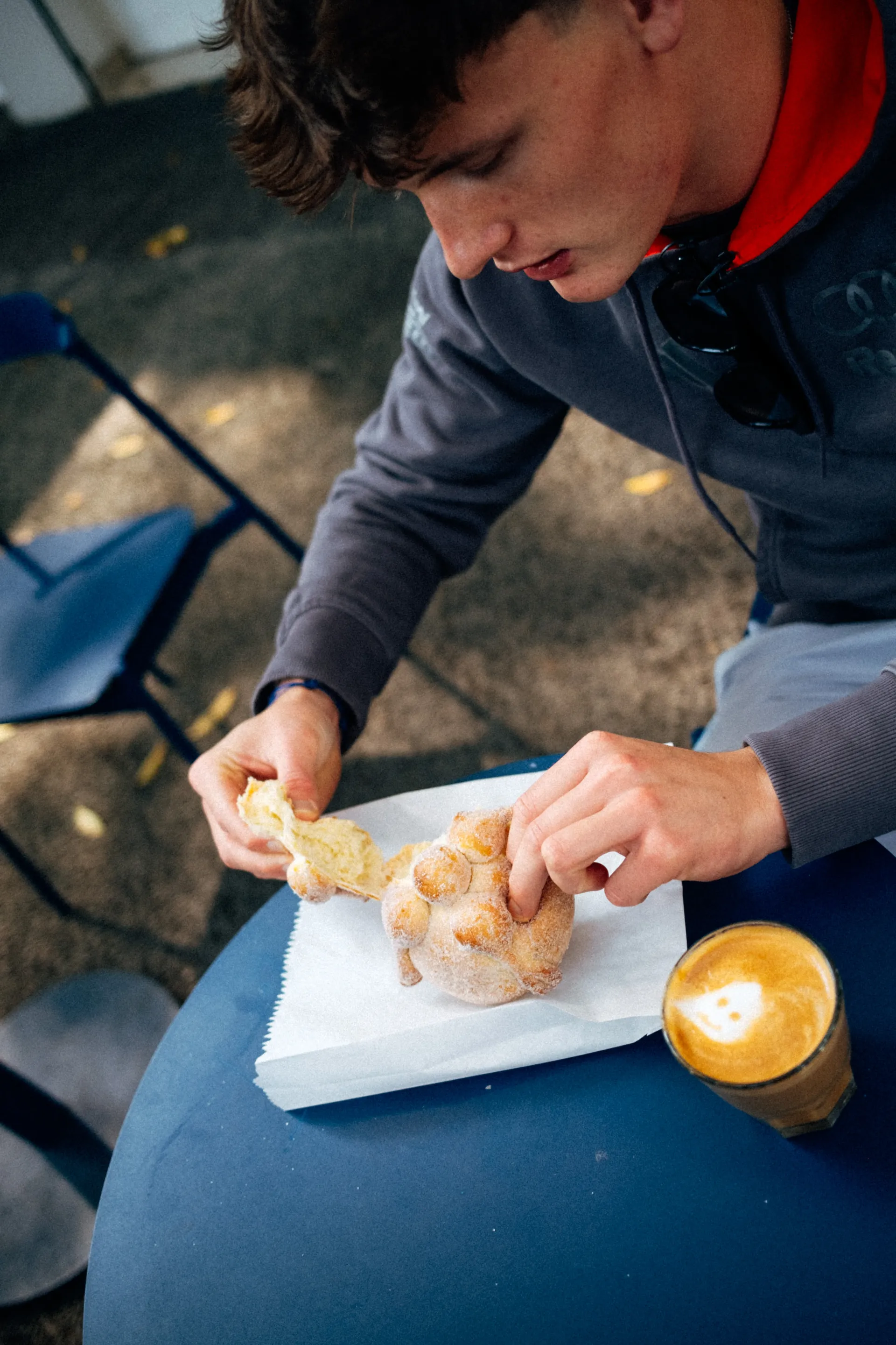 Freddie Slater tearing a pan de muerto next to a latte at a cafe table in Mexico City