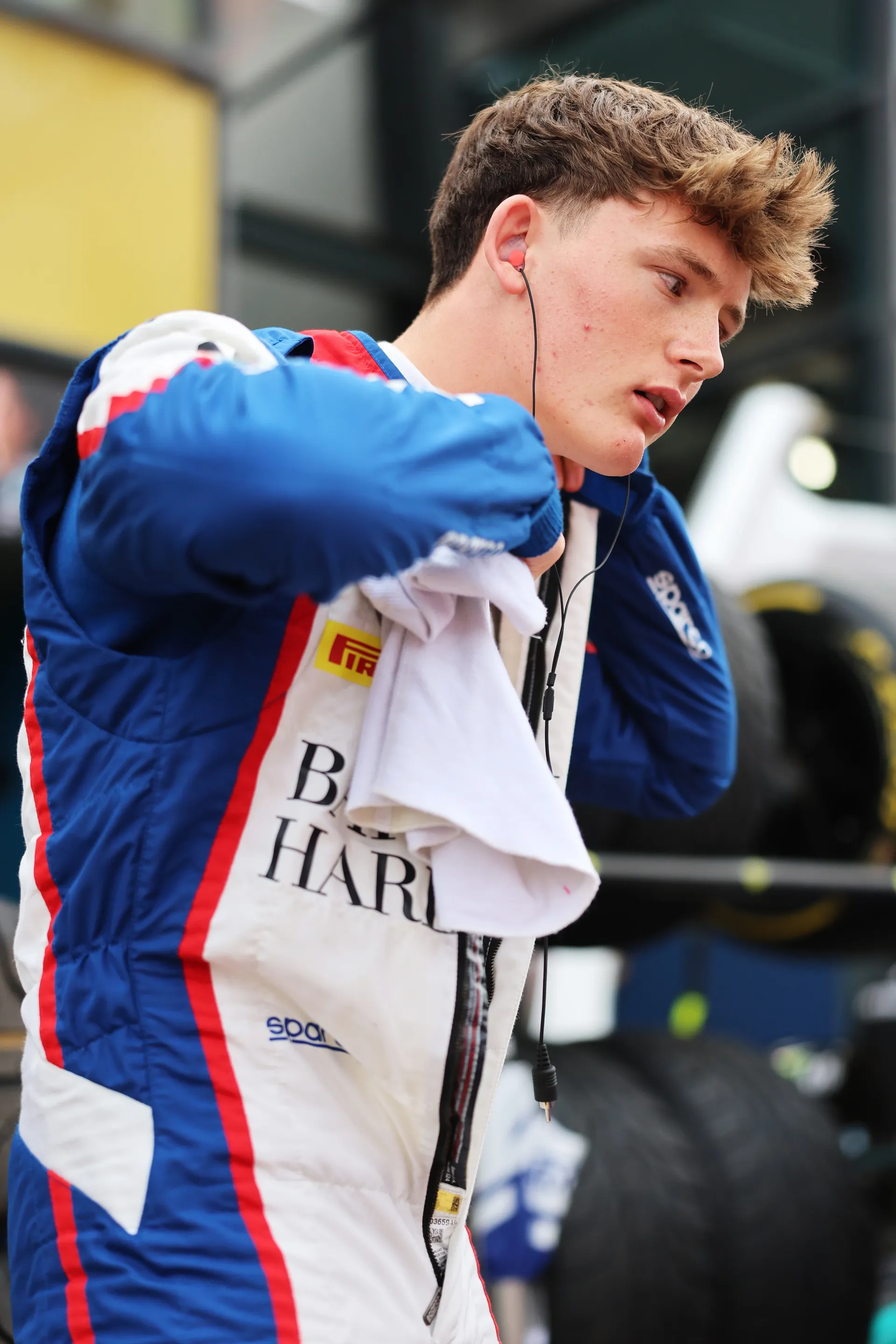 Freddie Slater putting on his race suit while wearing in ear headphones in the Formula 3 paddock