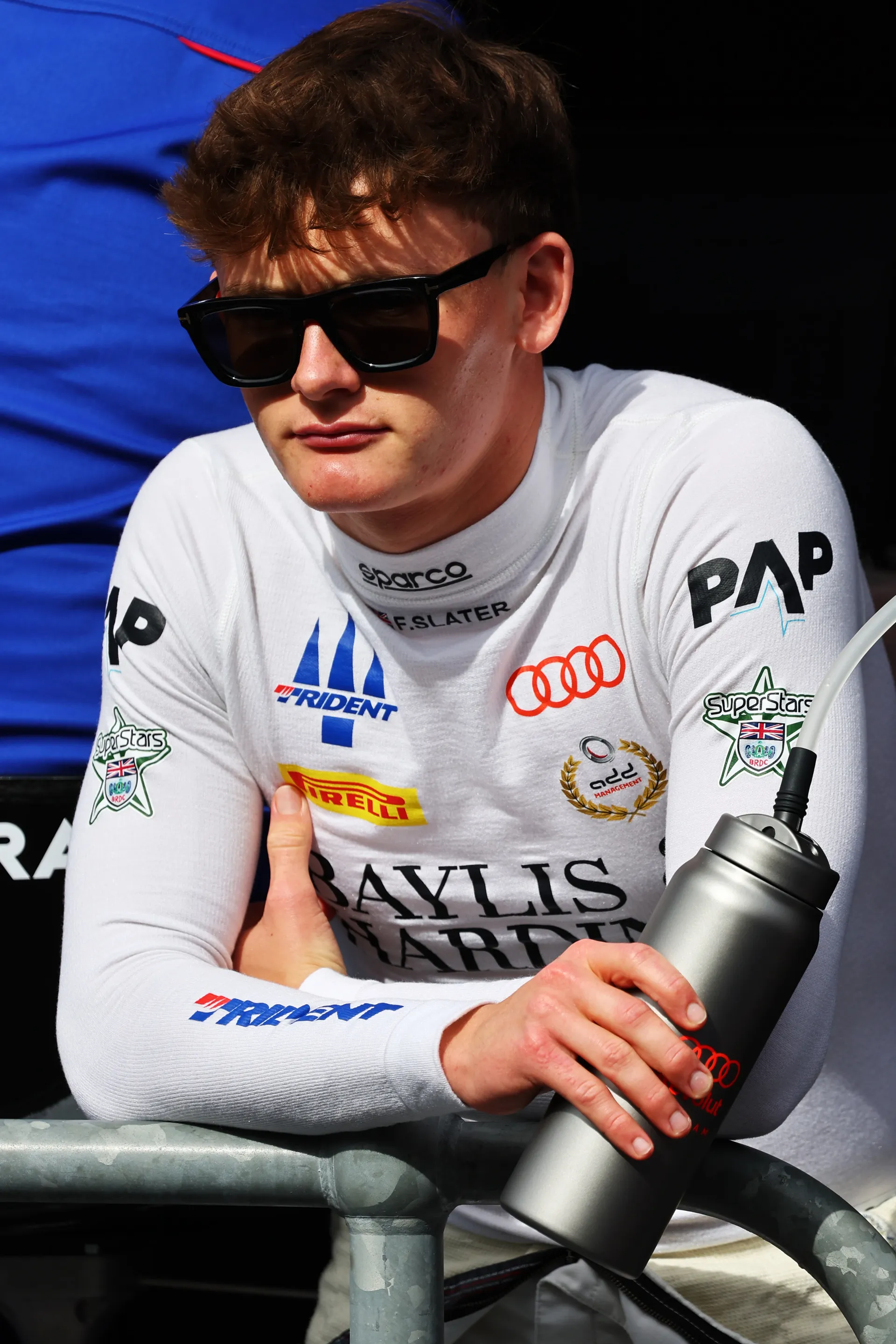 Freddie Slater leaning on a barrier holding a water bottle wearing Audi branded race base layer in the paddock