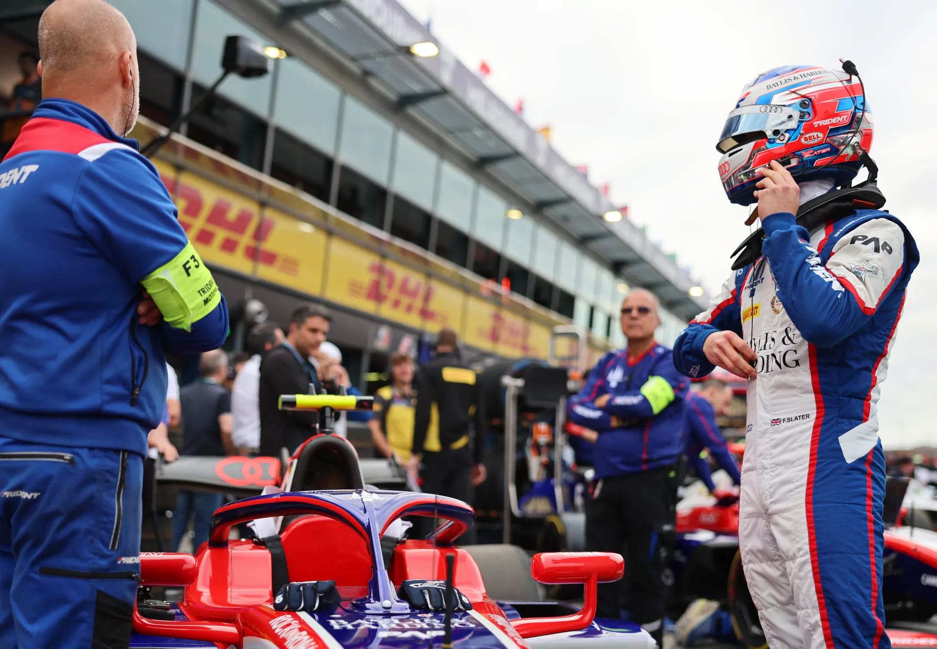 Freddie Slater adjusting his helmet next to his Formula 3 car in the pit lane before heading out