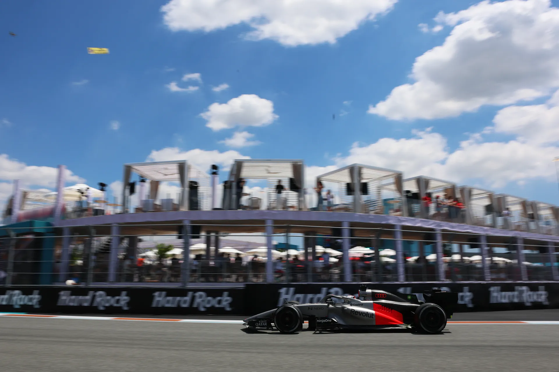 Audi Revolut F1® Team car driving past hospitality suites at Miami Grand Prix circuit under blue sky