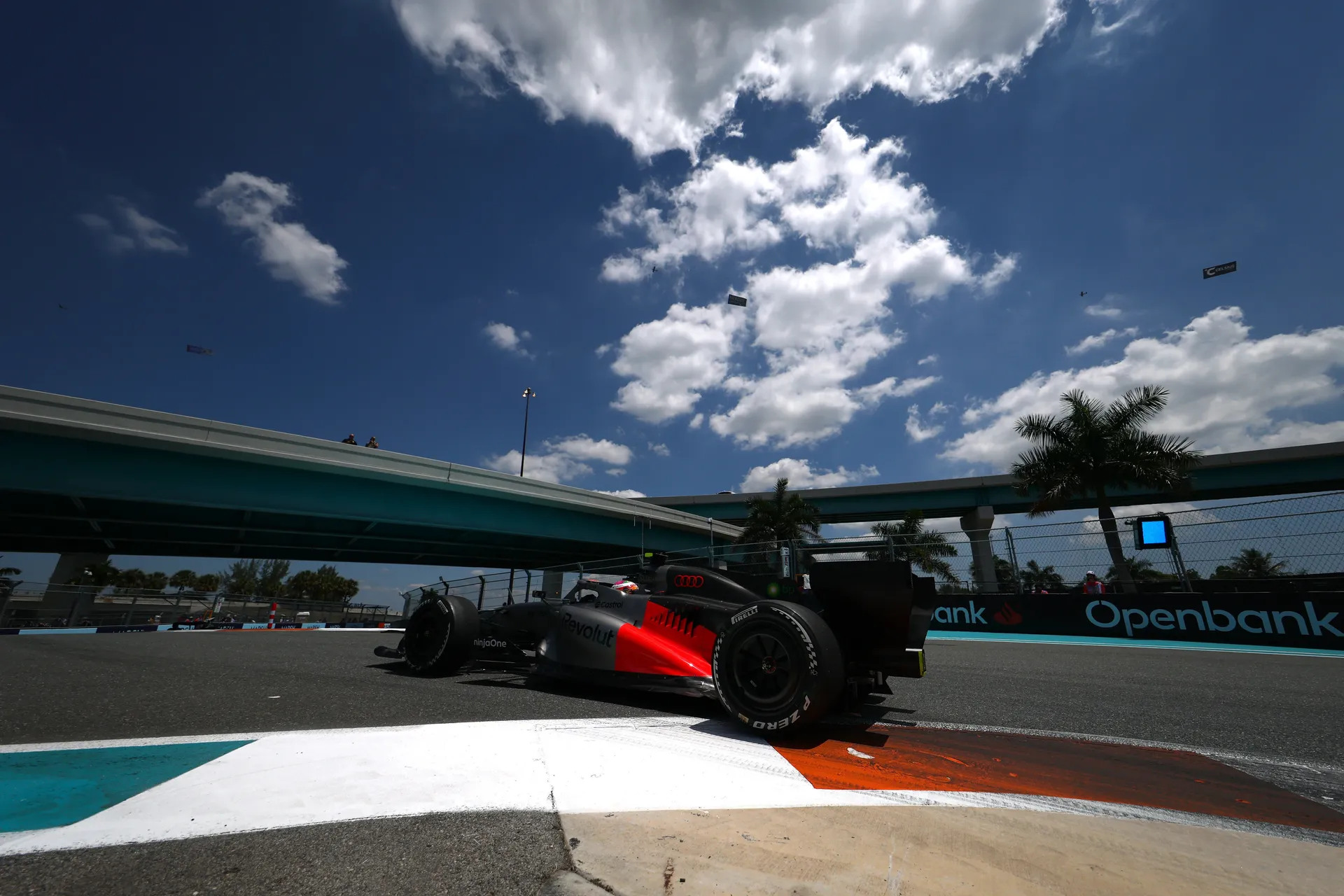 Audi Revolut F1® Team car riding over kerbs at Miami street circuit with highway bridges and palm trees in background