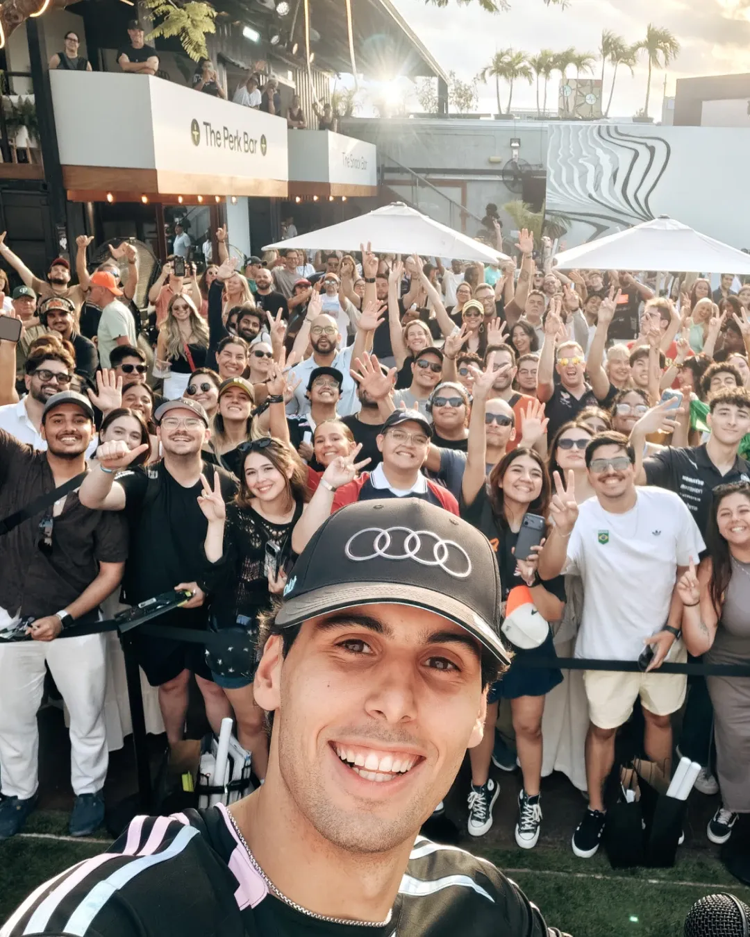 Gabriel Bortoleto takes a selfie with a large crowd of fans during the Audi Revolut F1® Team off track activation at MAPS Backlot in Miami, wearing the special adidas x Audi Revolut F1® Team Miami collection.