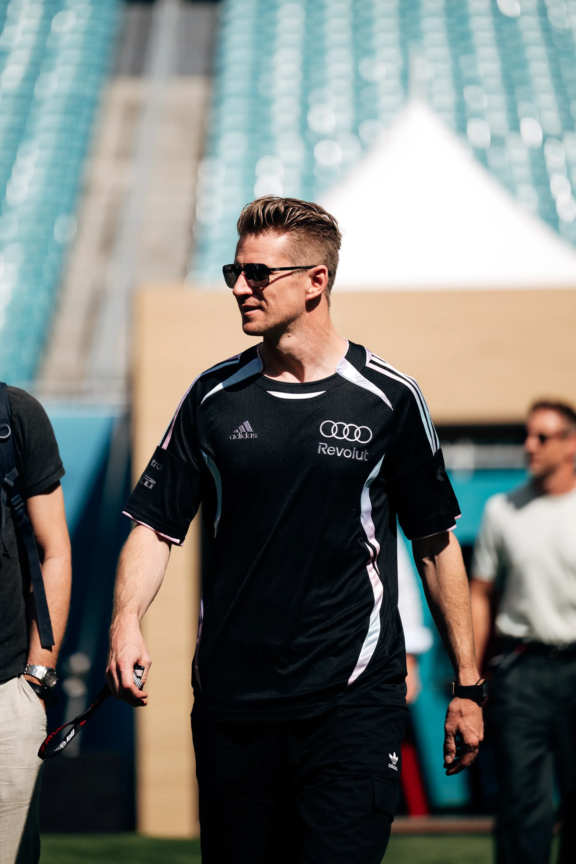Nico Hulkenberg arriving at track in sunglasses and an adidas x Audi Revolut F1® Team shirt, walking through the paddock area.