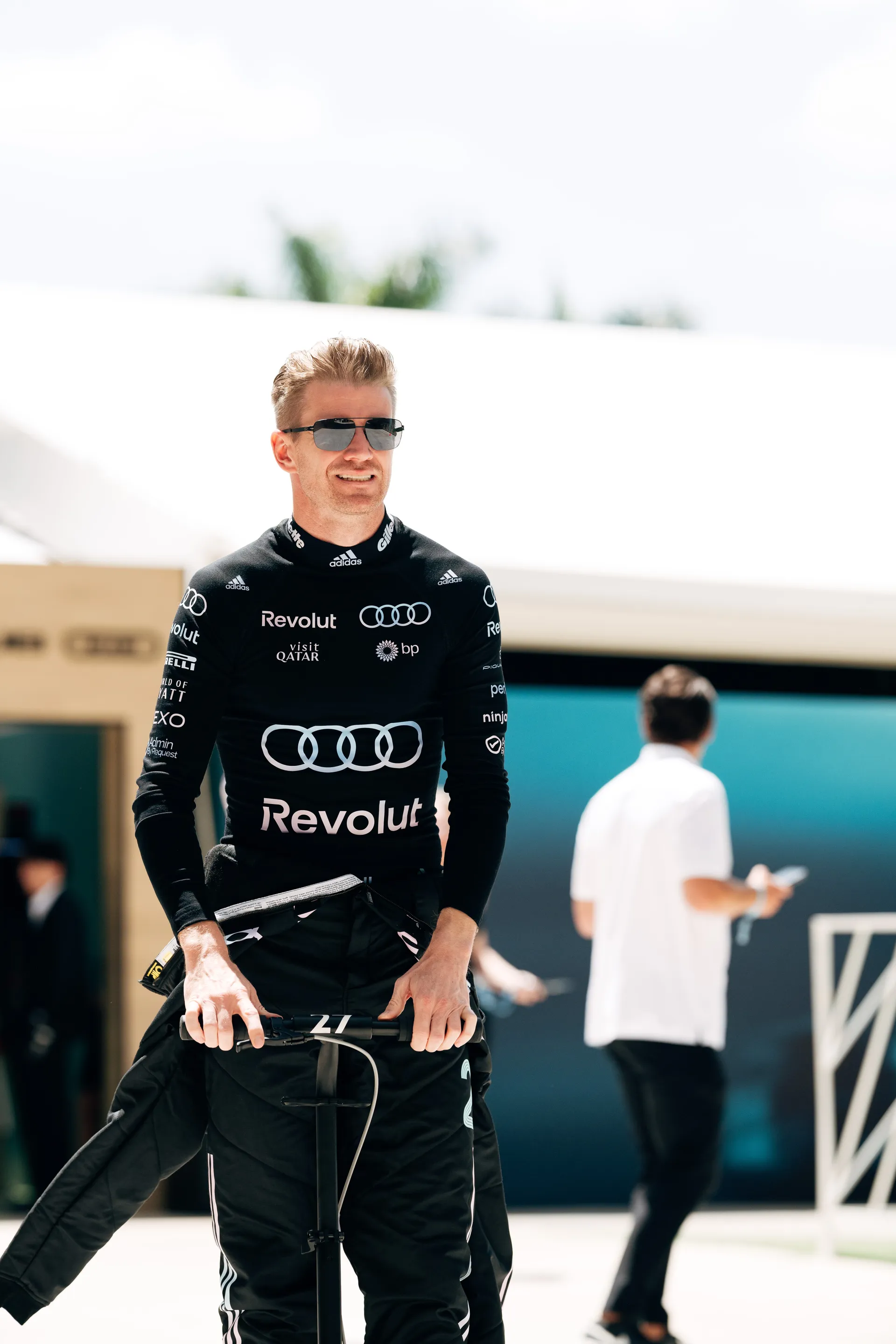 Nico Hulkenberg arrives at the track in Audi Revolut F1® Team racewear and sunglasses, with the number 27 visible on the handlebar.