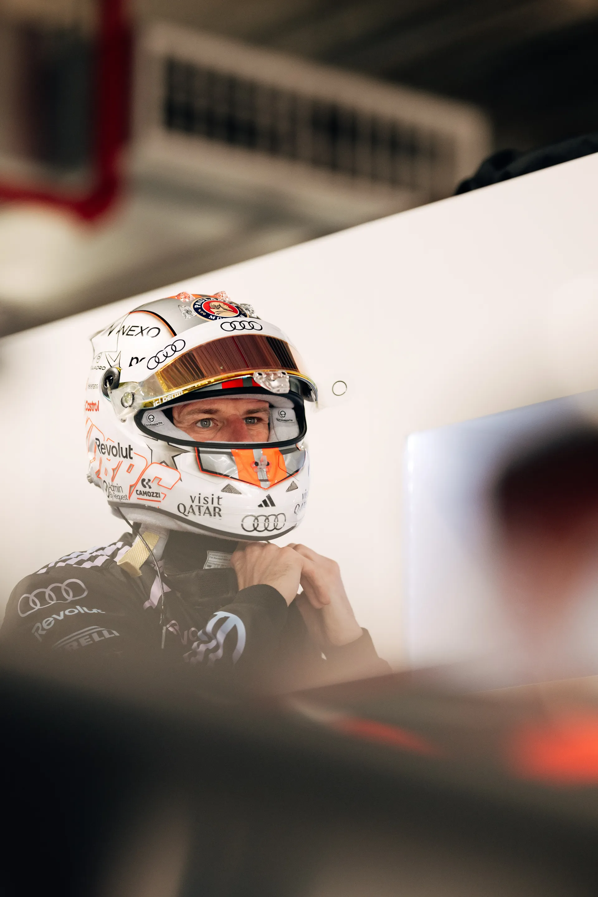 Nico Hulkenberg secures his helmet strap in the garage, focused ahead as he prepares to drive for Audi Revolut F1® Team.