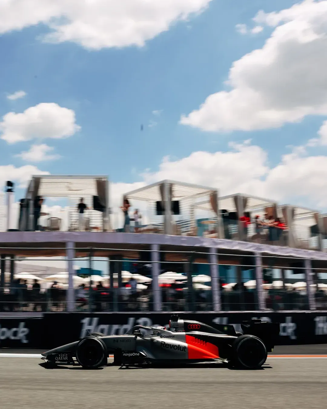 Audi Revolut F1® Team car number 27, driven by Nico Hulkenberg, speeds past the Miami paddock buildings during an on track session under a bright blue sky.