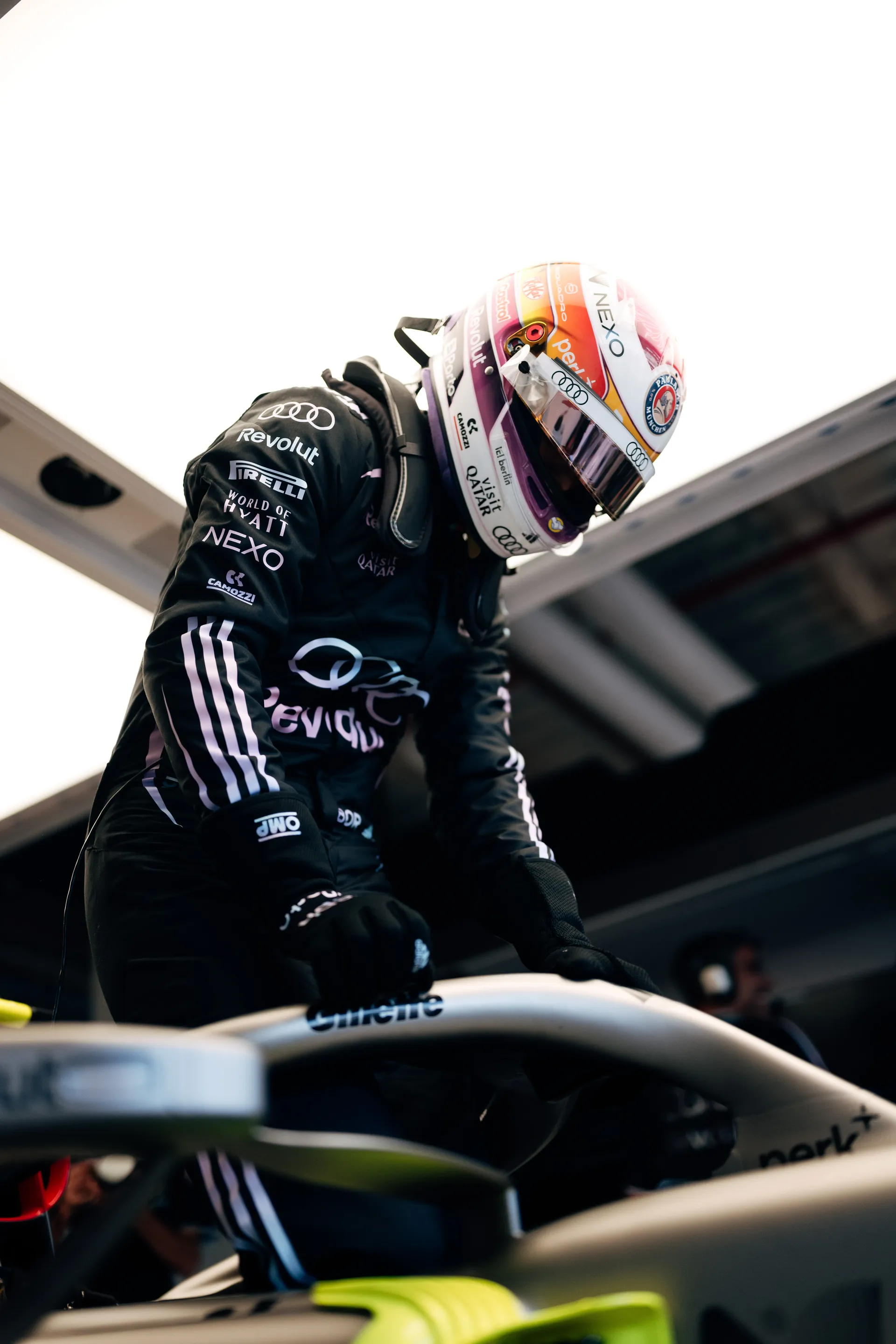 Low angle view of Gabriel Bortoleto in full Audi Revolut F1® Team race gear and special Miami edition helmet leaning over the Formula 1 car inside the garage.