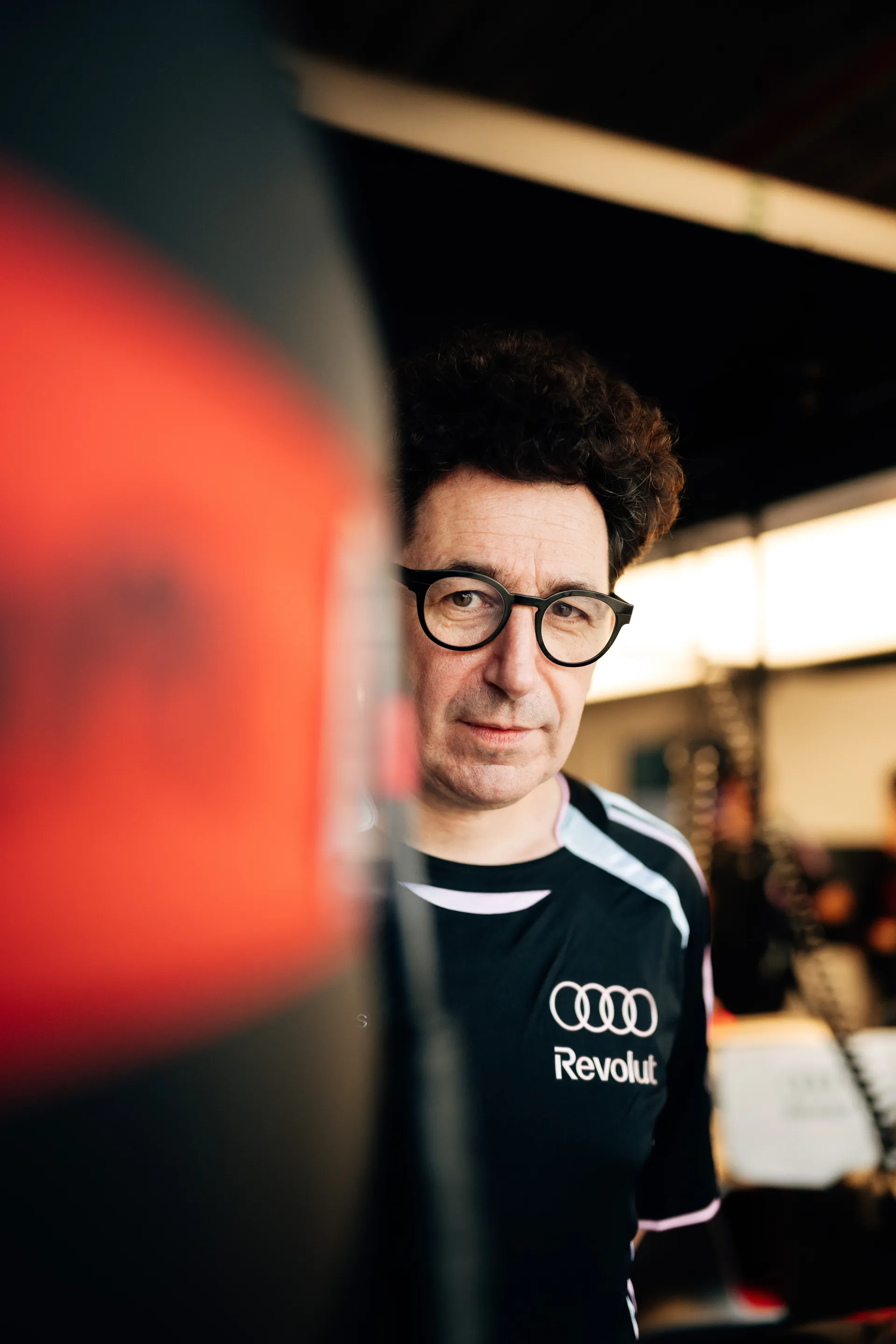 Portrait of Mattia Binotto of  Audi Revolut F1® Team in team kit and glasses looking toward the camera inside the garage.
