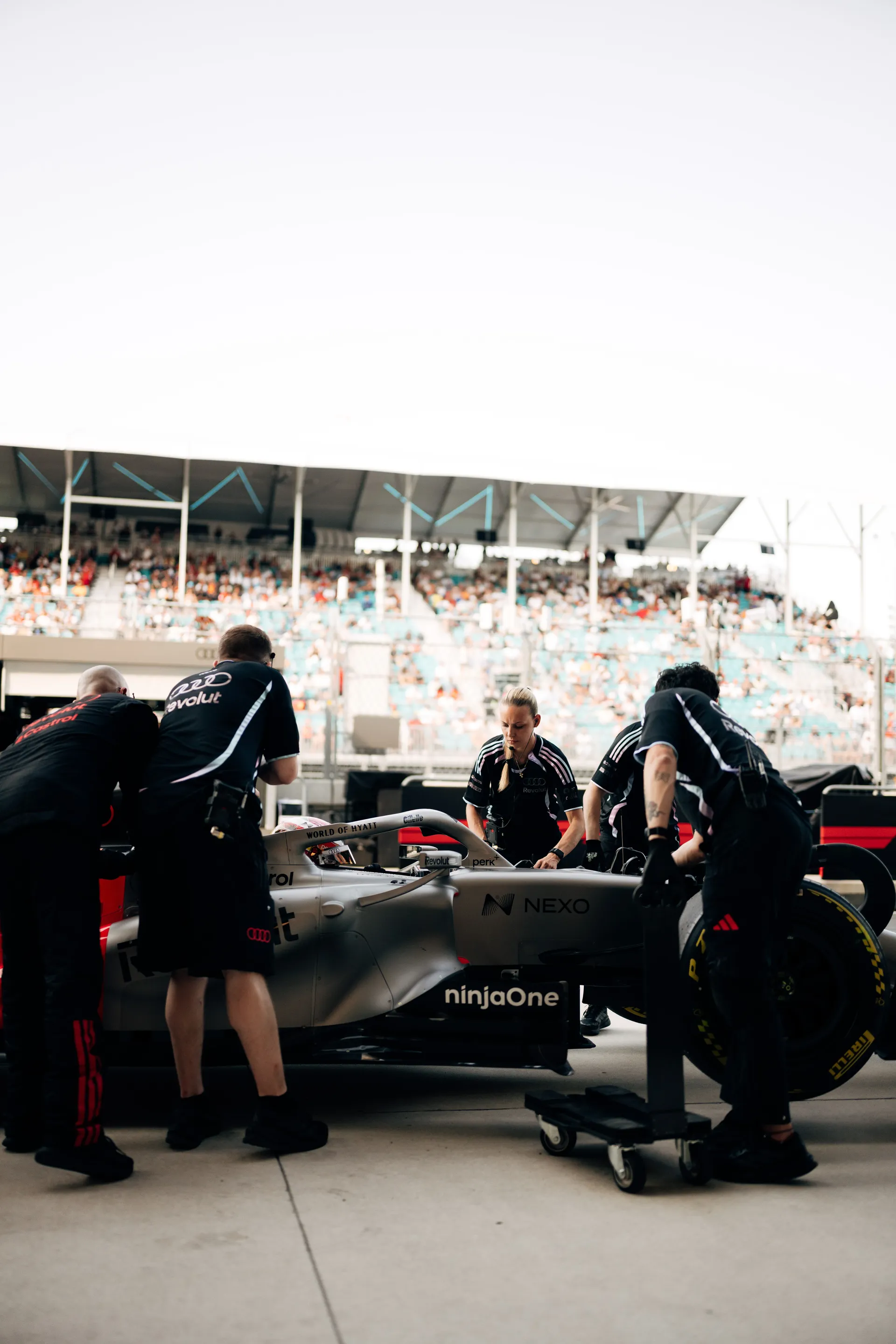 The Audi Revolut F1® Team Formula 1 car is pushed into position in the pit lane garage while crew members work around it in front of packed grandstands.
