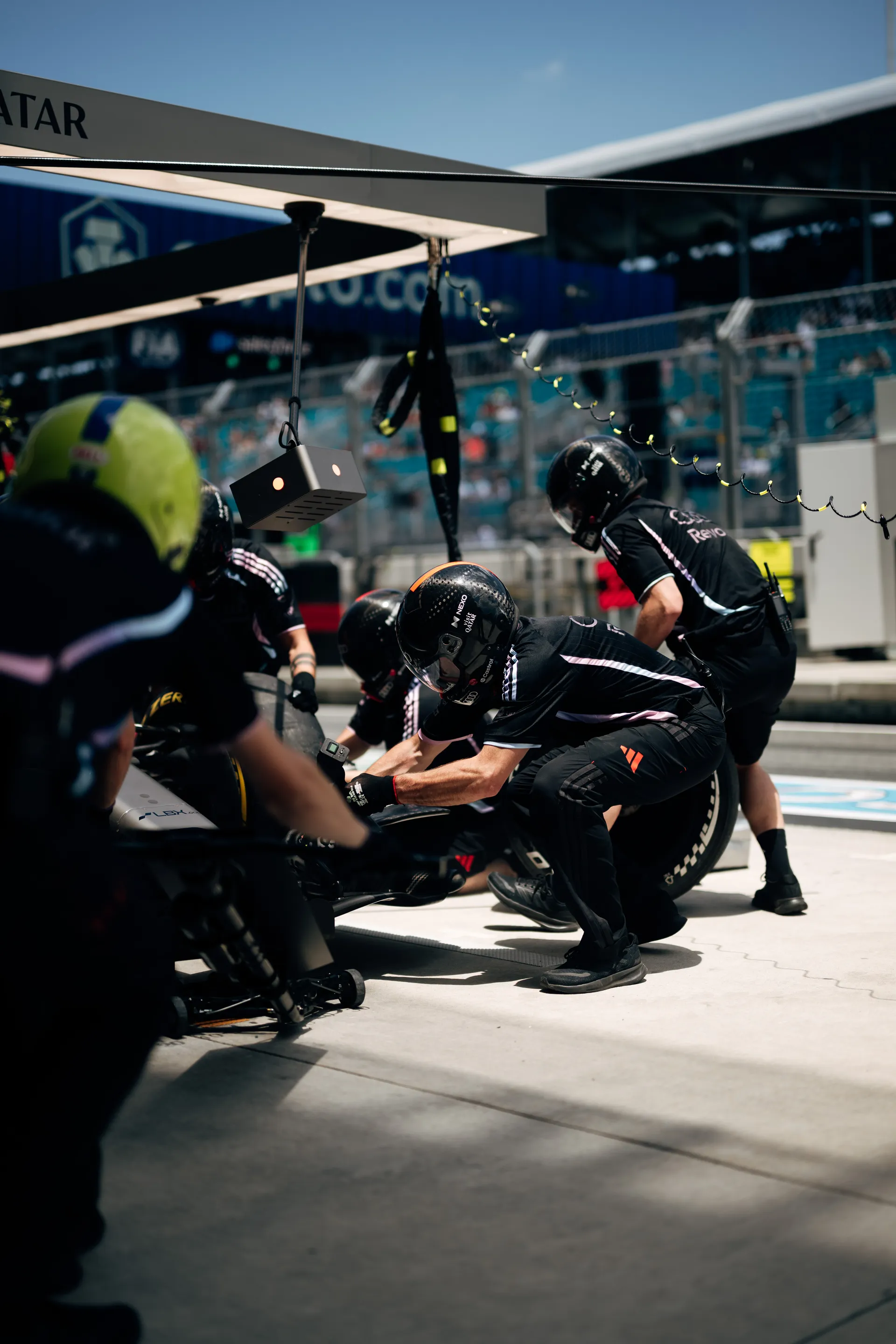 Another angle of the pit stop rehearsal, with multiple crew members crouched around the car in bright Miami sunlight.