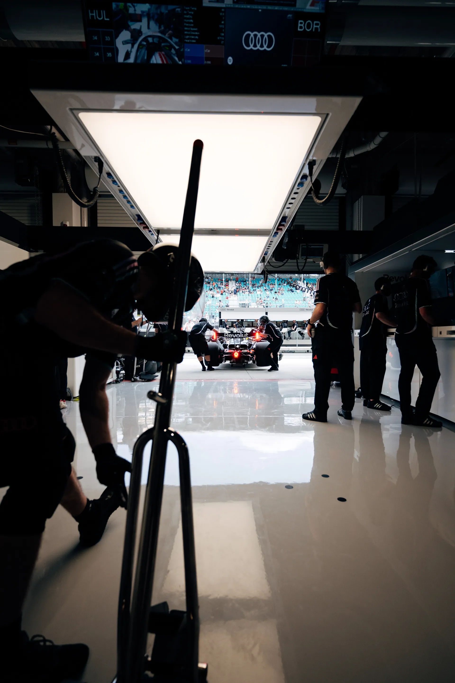 Long view through the garage toward the pit lane as crew members prepare to release the car, with the rear light glowing red.