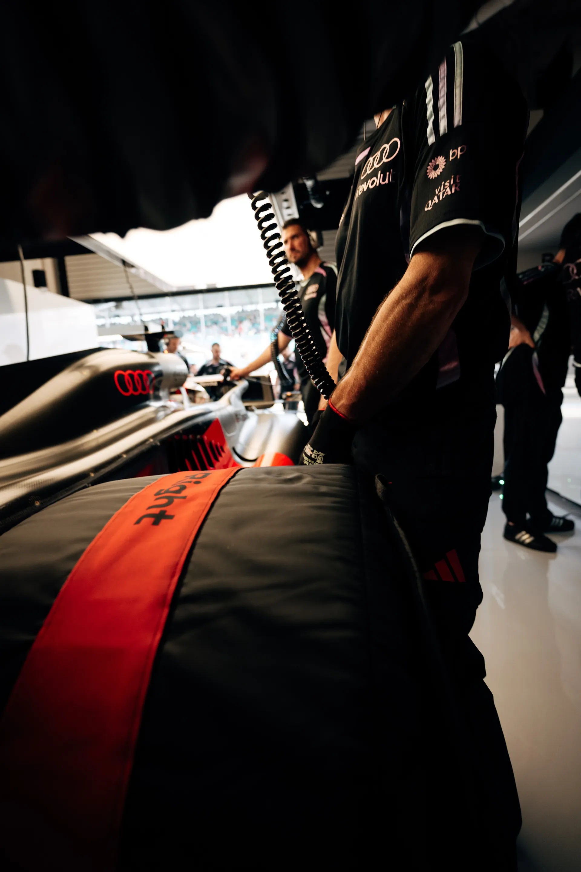 Close-up inside the garage with a tire blanket in the foreground and the Audi Revolut F1® Team car partially visible behind it.