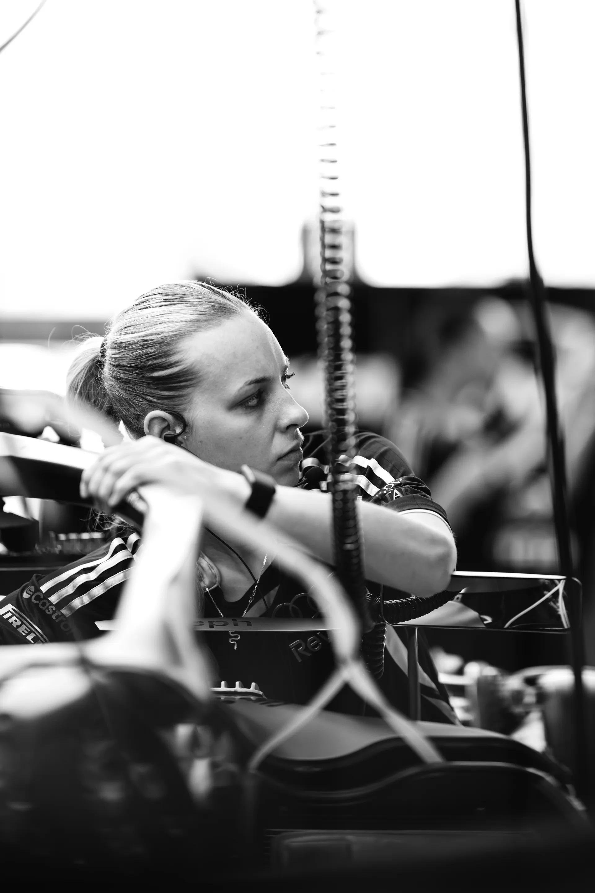 Female Audi Revolut F1® Team mechanic leans over the car, focused on adjustments with headset in place.