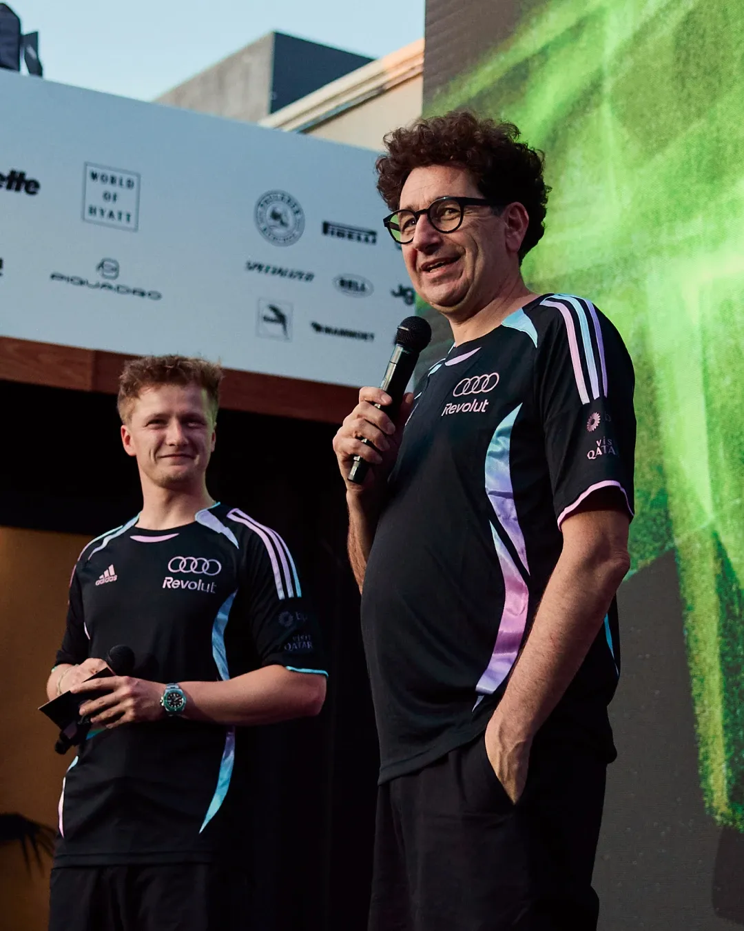 Audi Revolut F1® Team Mattia Binotto speaking on stage with a microphone during the MAPS backlot activation, with a team member standing beside him