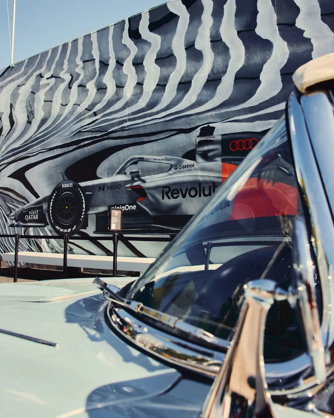 Audi Revolut F1® Team show car installation positioned in front of a large mural, with a vintage car in the foreground