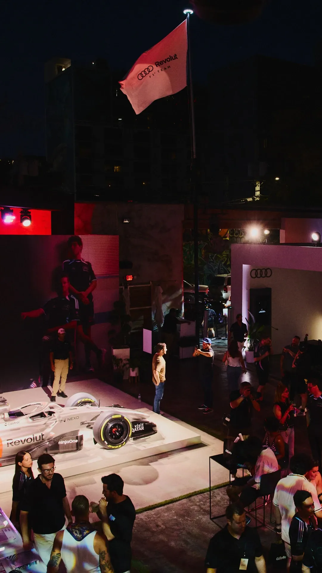 Audi Revolut F1® Team branded flag raised above the MAPS backlot venue at night with attendees gathered below