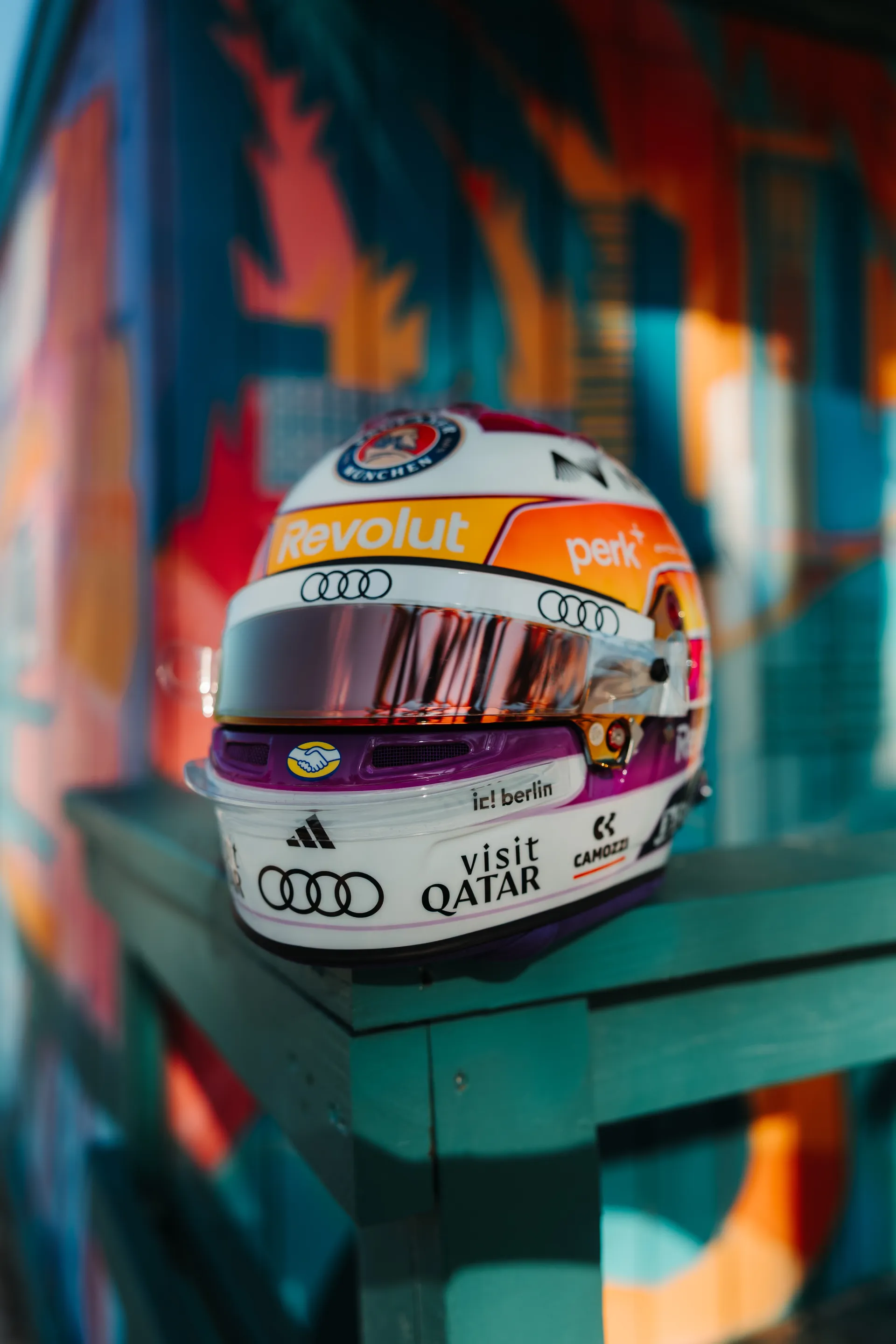 Three quarter front view of Gabriel Bortoleto’s special Miami edition race helmet on a turquoise lifeguard stand, set against a vibrant Miami style mural.