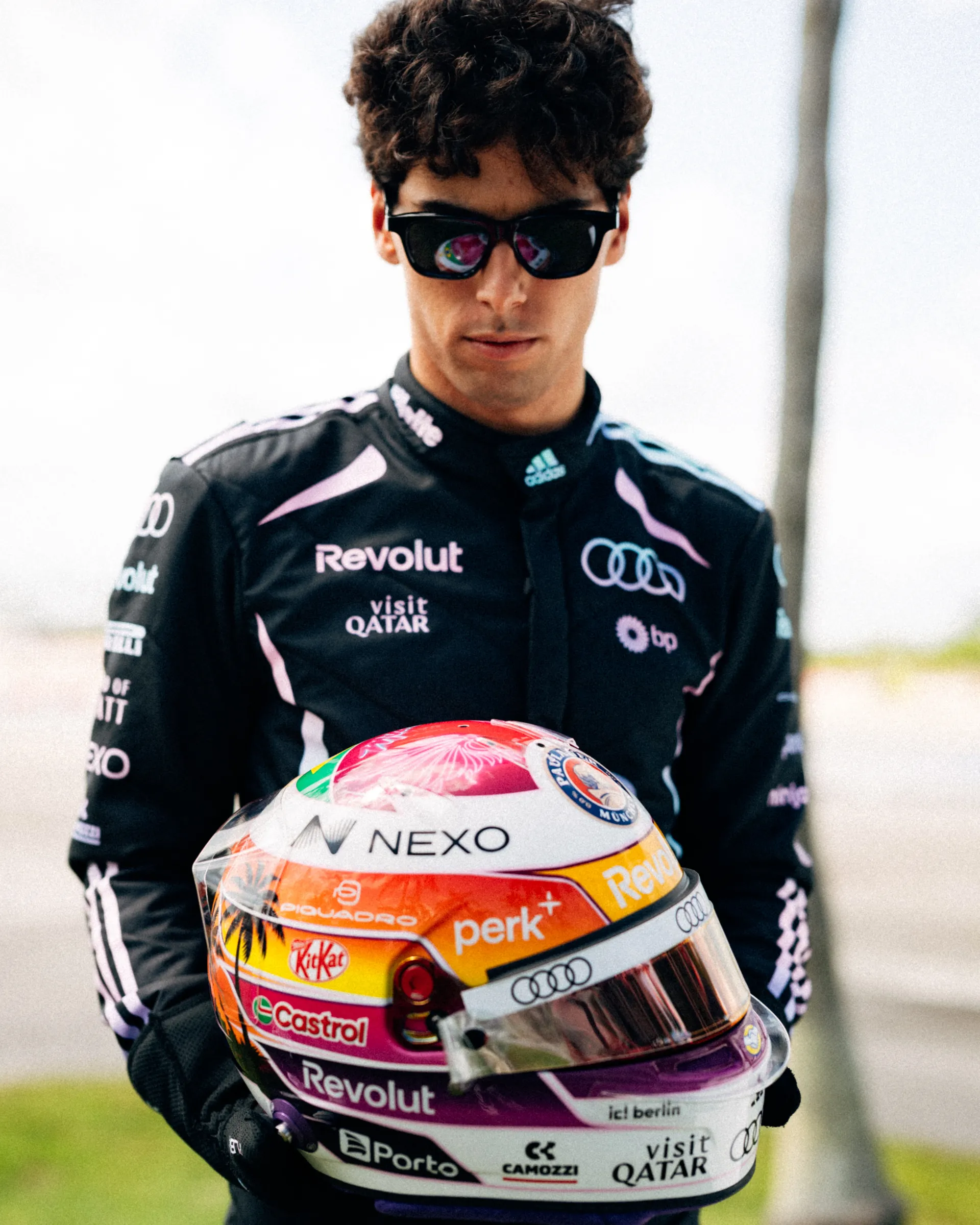 Close portrait of Gabriel Bortoleto in sunglasses and Audi Revolut F1® Team Miami race suit, holding his special Miami edition helmet.