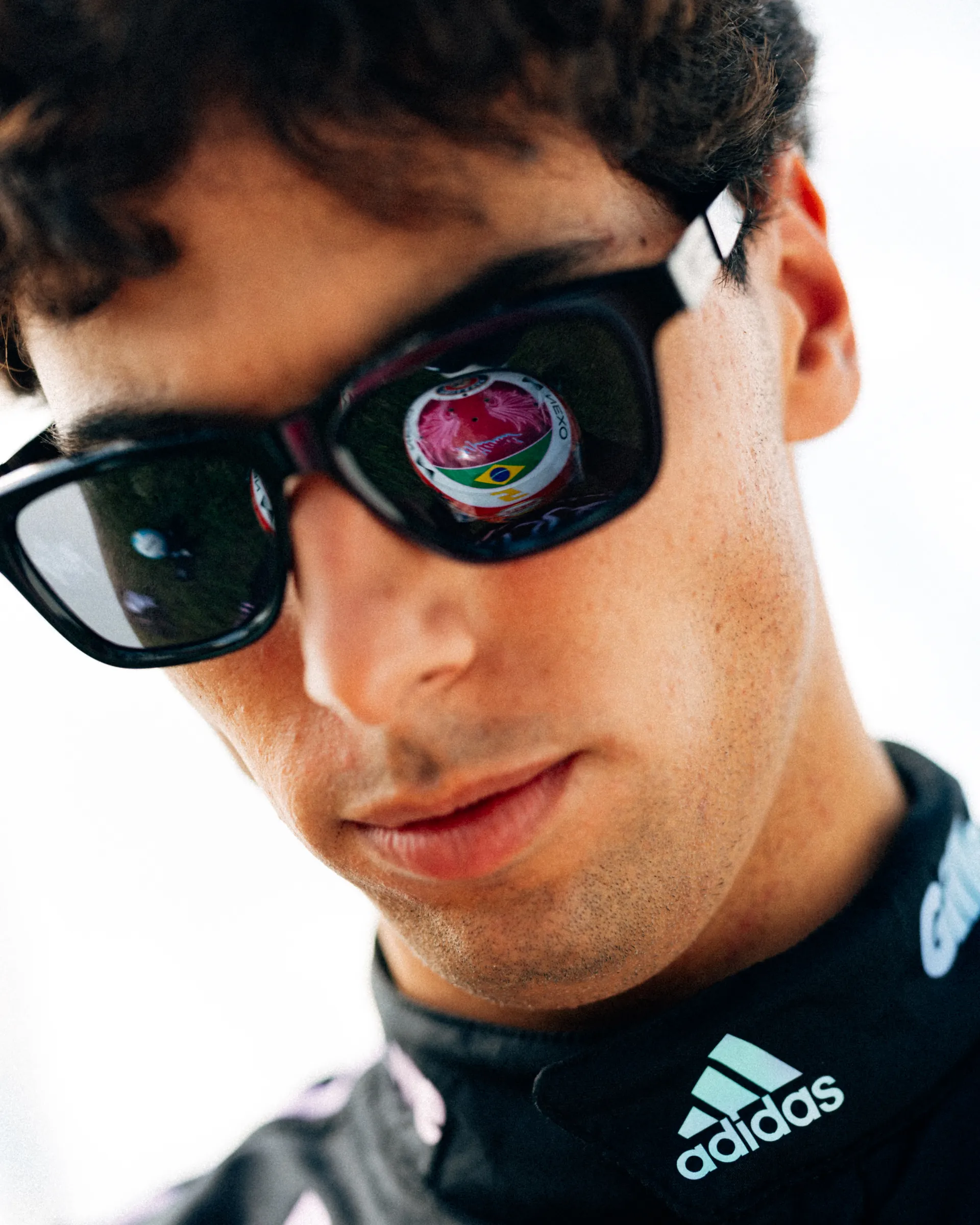 Extreme close up of Gabriel Bortoleto wearing sunglasses, with the pink crown design of his special Miami edition helmet reflected in the lens.