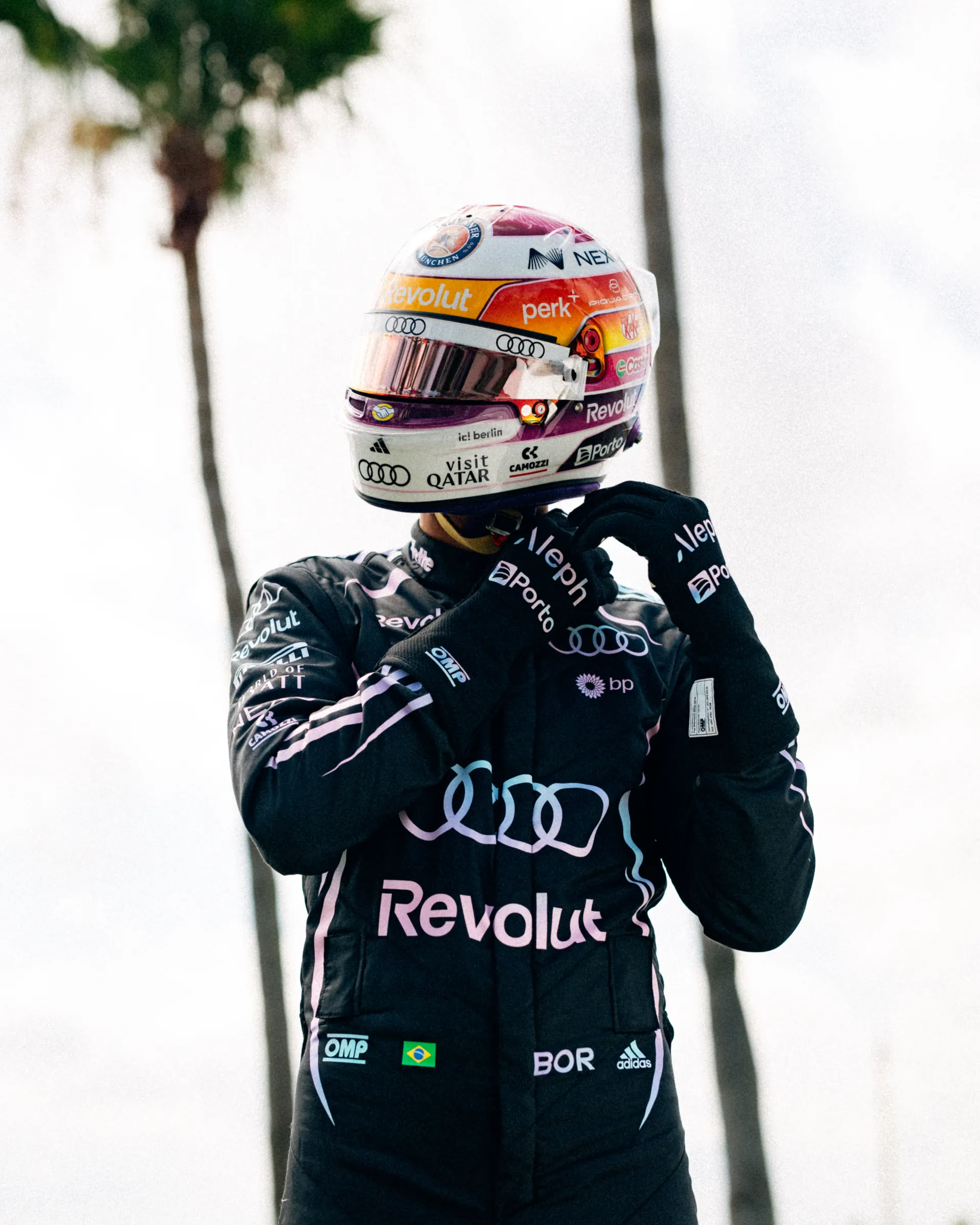 Gabriel Bortoleto fastening his special Miami edition race helmet while wearing the Audi Revolut F1® Team Miami race suit under palm trees.