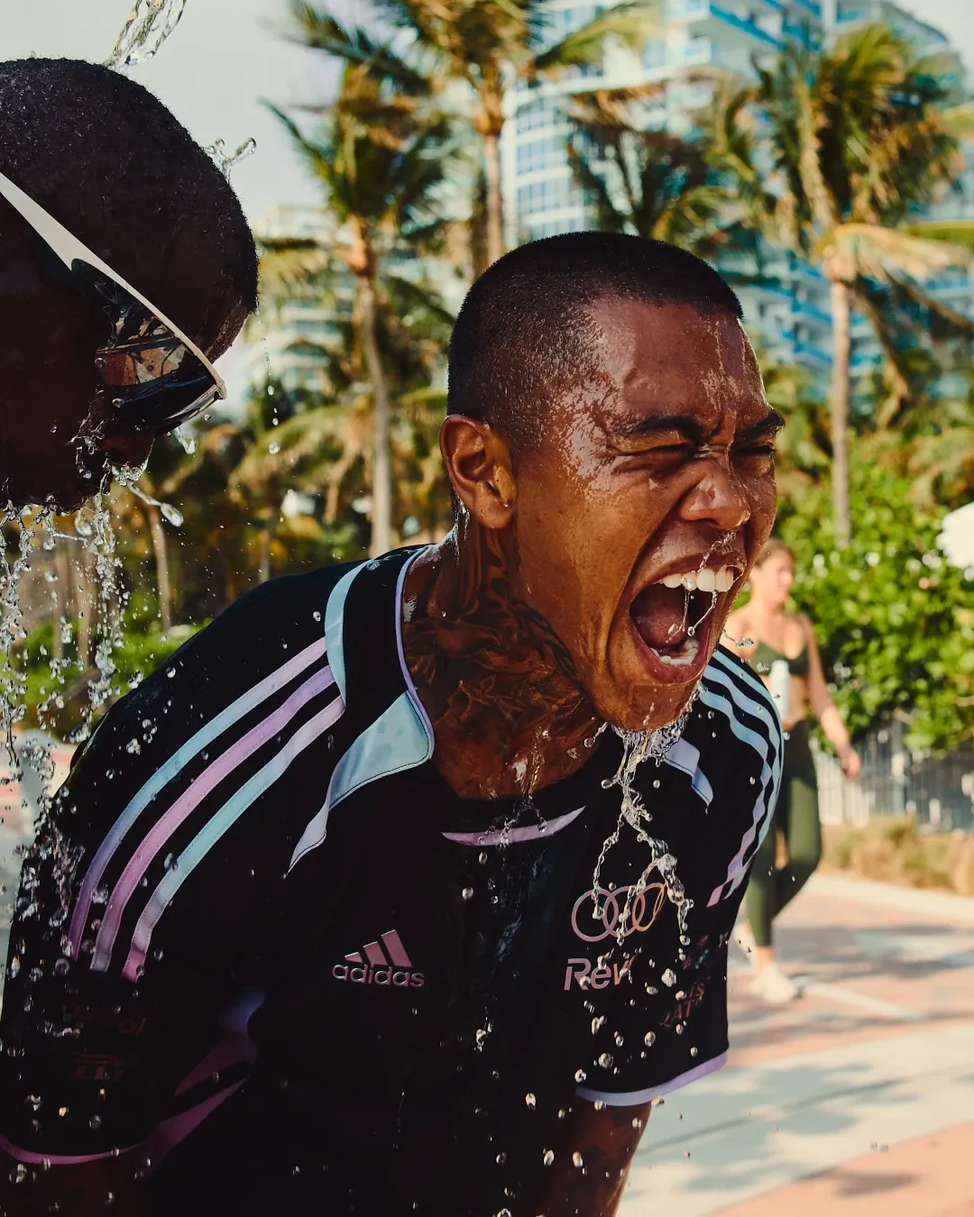 Participant reacts as water is poured over him during the adidas social run in Miami, wearing the special adidas Audi Revolut F1® Team Miami collection.