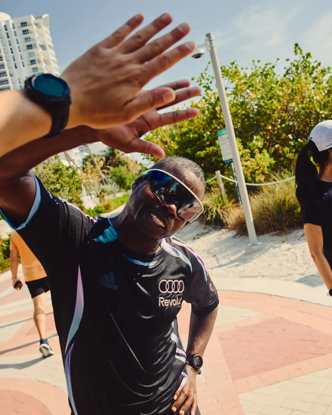 Runner smiles and waves at the camera during the adidas social run in Miami, wearing the special adidas Audi Revolut F1® Team Miami collection.