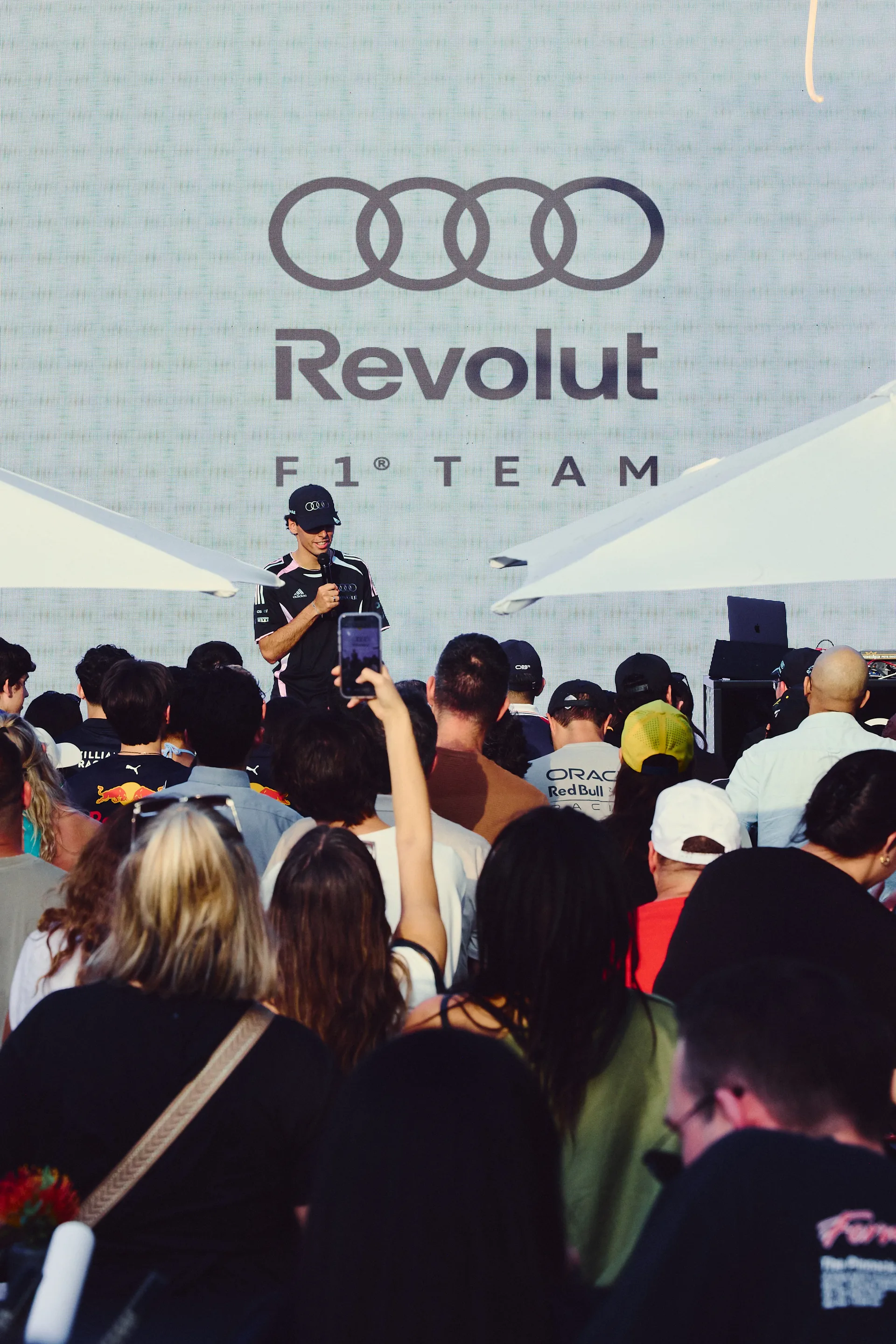 Audi Revolut F1® Team driver Gabriel Bortoleto addresses a large crowd on stage during Miami activation, with fans filming and reacting in front of branded backdrop.