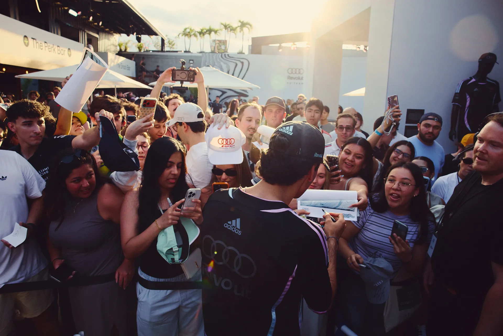 Audi Revolut F1® Team driver Gabriel Bortoleto signs autographs for a dense crowd of fans, with high interaction and mobile-first behavior visible.