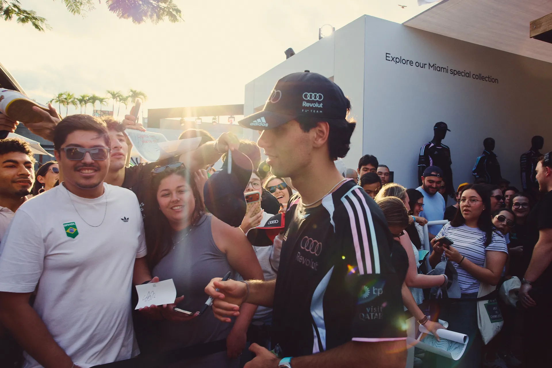 Audi Revolut F1® Team driver Gabriel Bortoleto interacts with fans during autograph session, surrounded by a diverse and engaged audience.