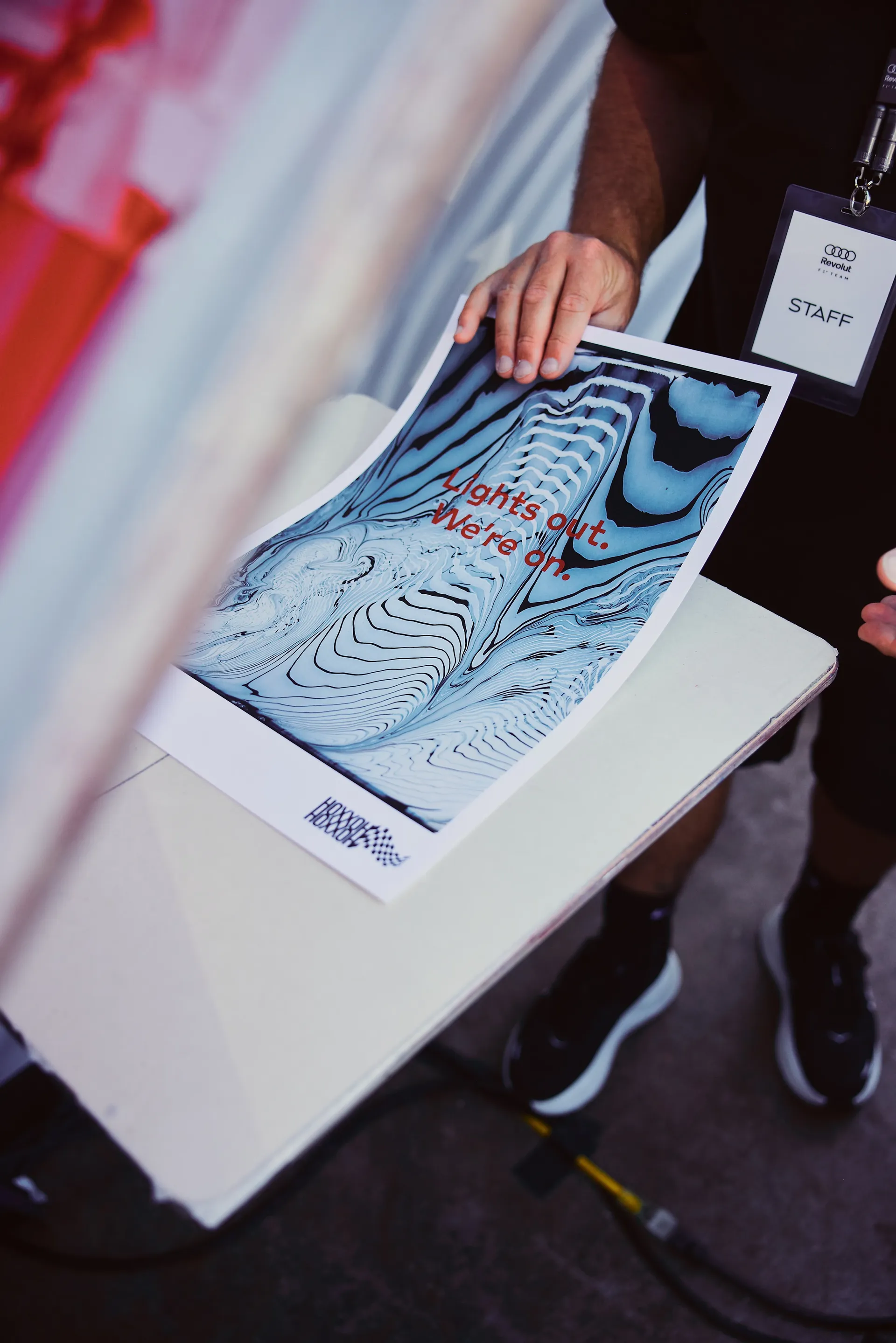 Staff member holding a printed artwork with “Lights out. We’re on.” slogan, representing campaign creative within activation space.