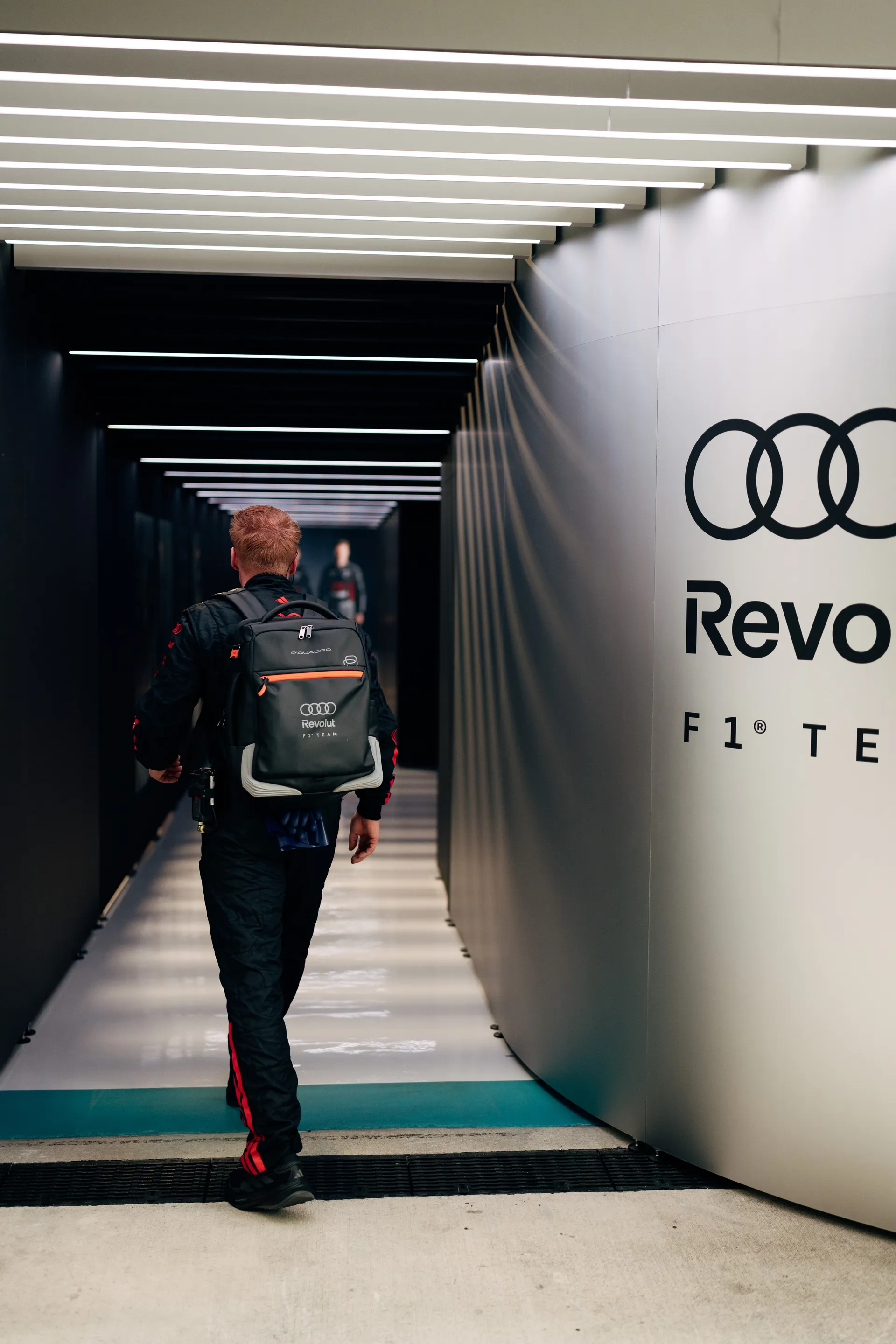 Audi Revolut F1® Team crew member walking through the paddock tunnel carrying a team backpack toward the garage