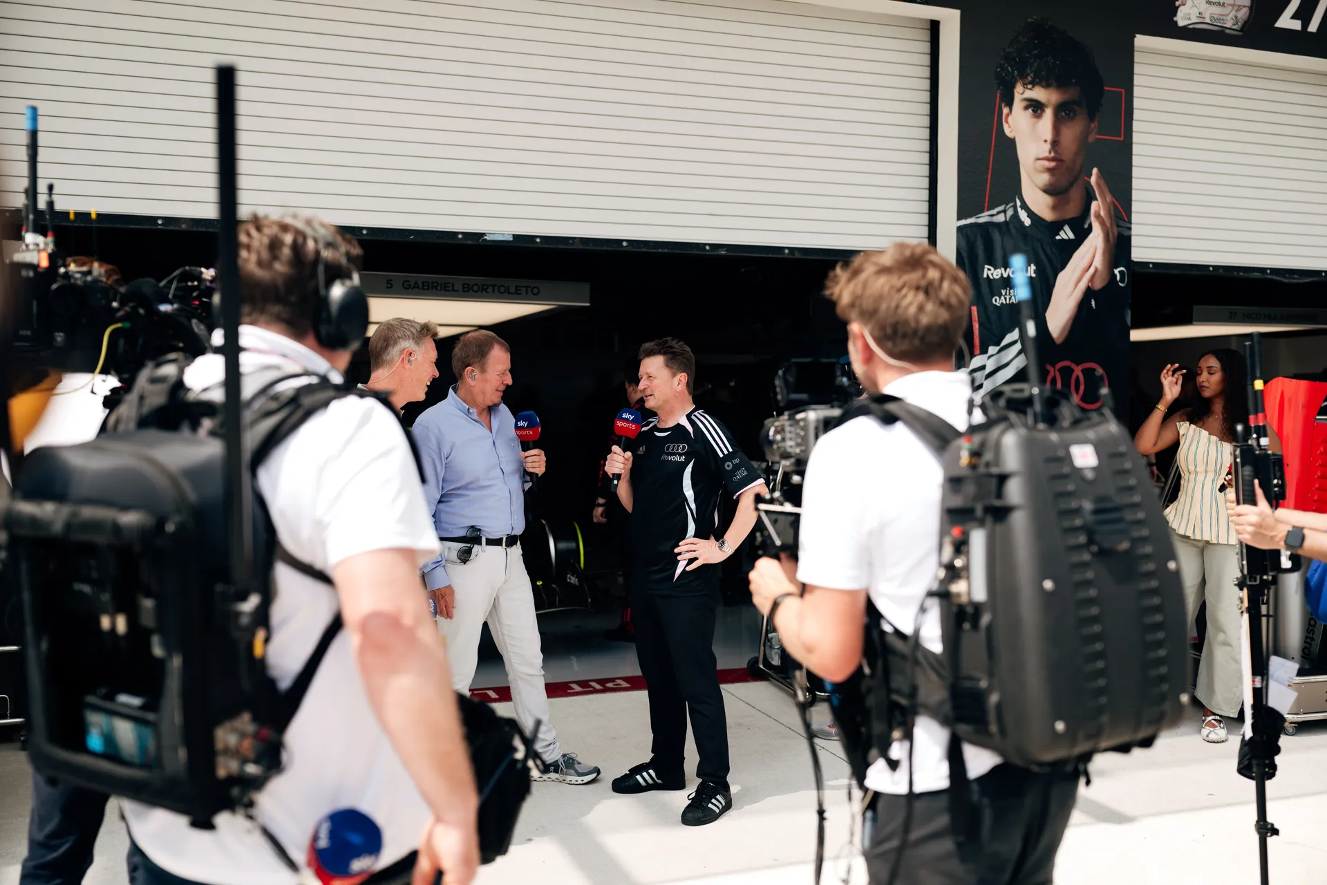 Audi Revolut F1® Team representative being interviewed by broadcast media in front of the garage with camera crew surrounding