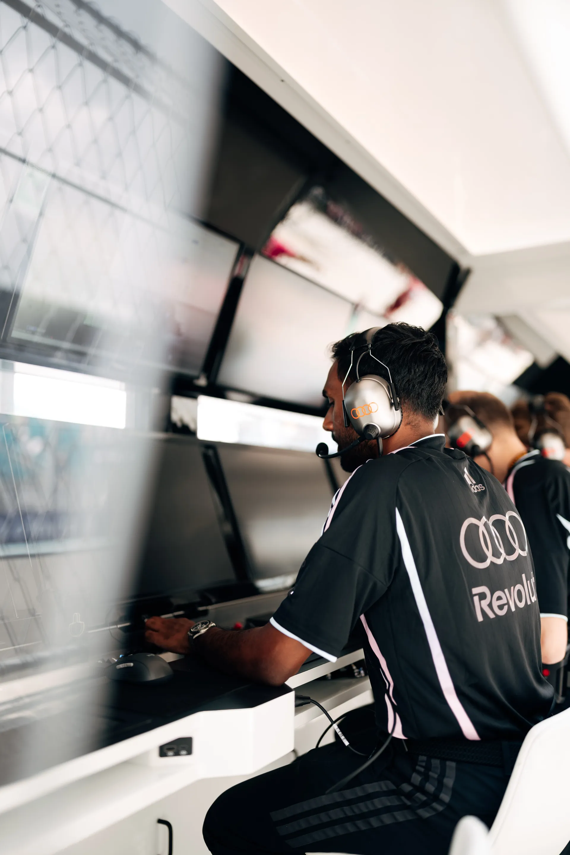 Audi Revolut F1® Team engineers working on laptops with headsets inside the garage monitoring live race data