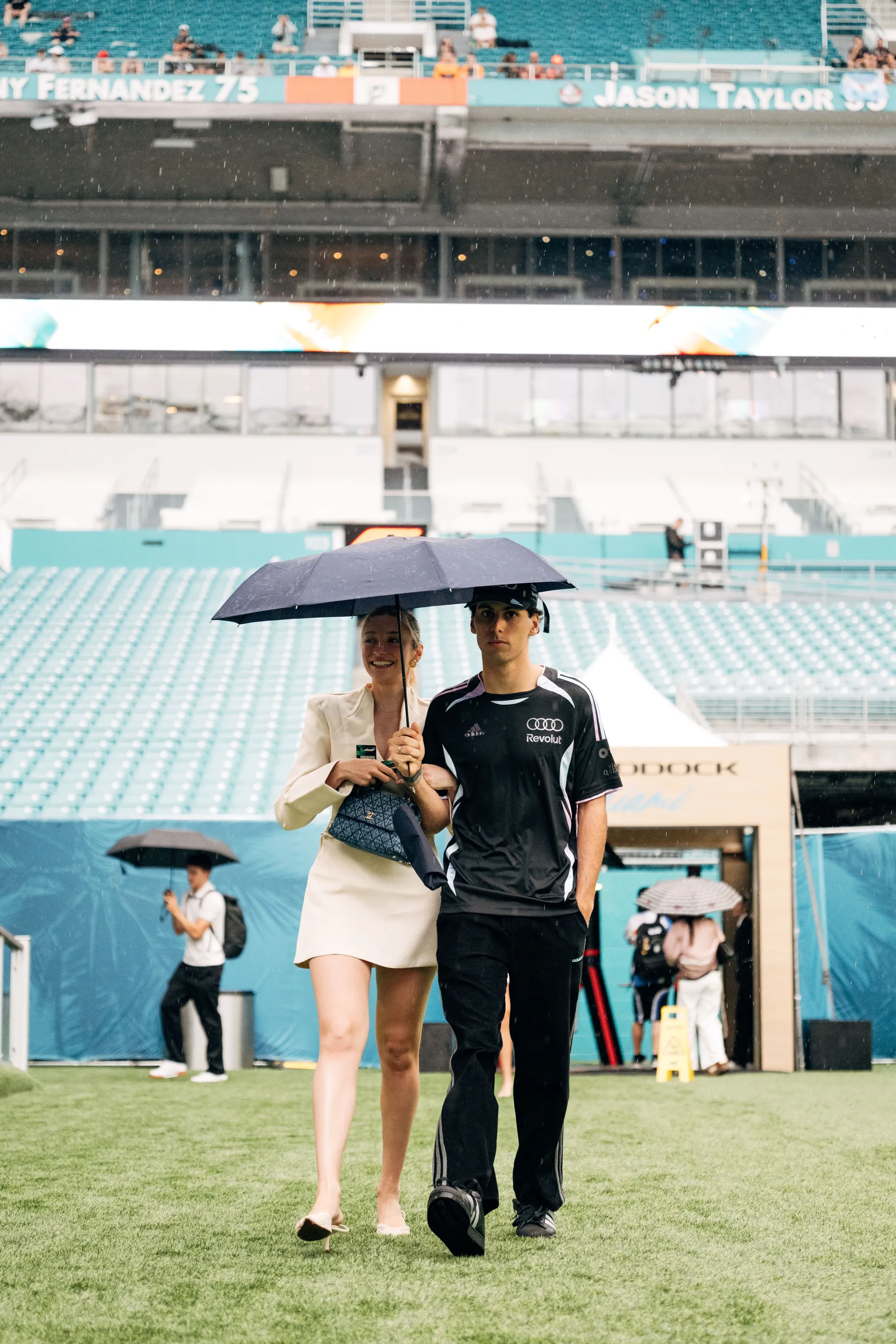 Gabriel Bortoleto arrives with a guest under an umbrella at the Miami International Autodrome ahead of the 2026 Miami Grand Prix sessions.