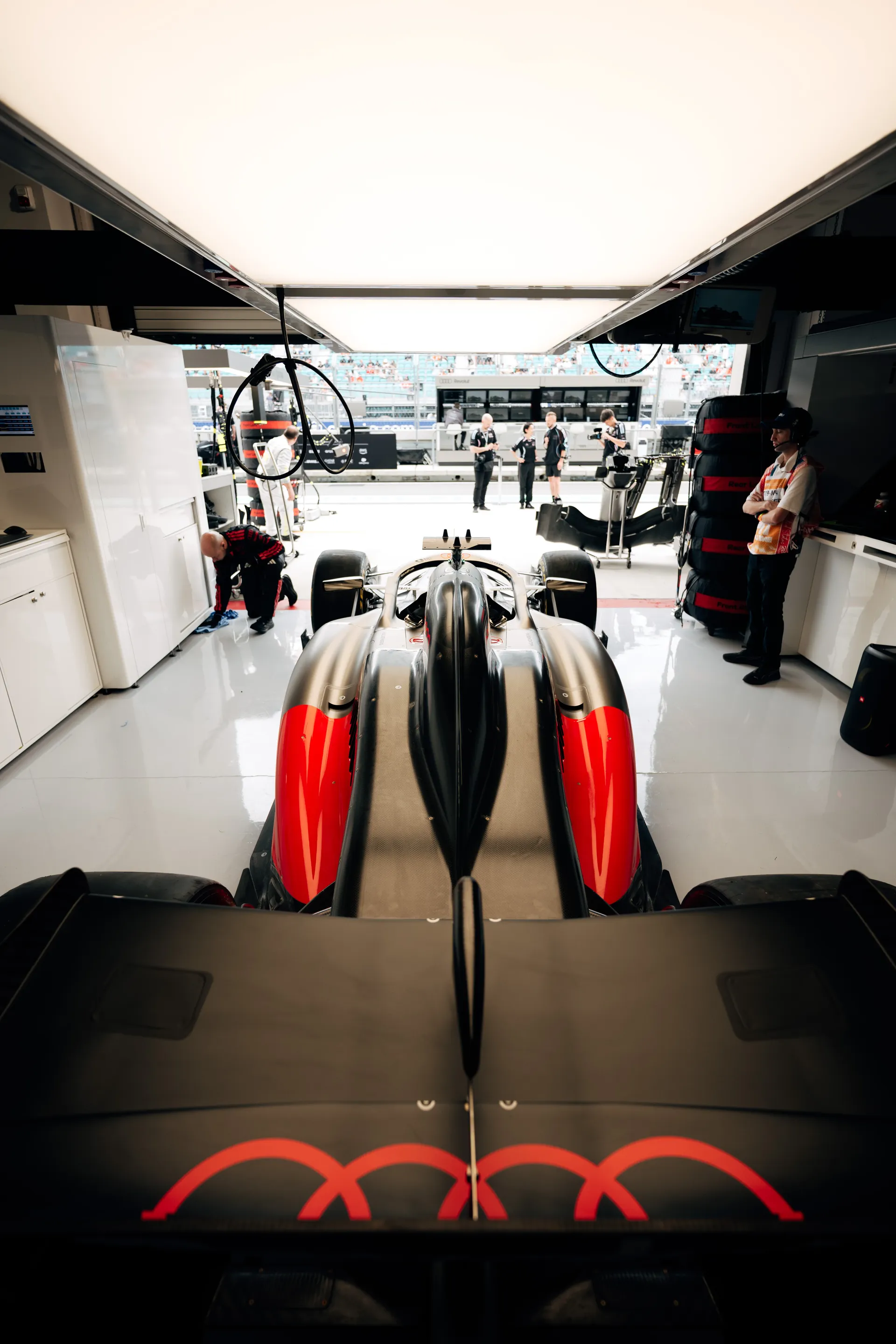 Rear view of an Audi Revolut F1® Team car inside the garage, positioned under bright overhead lighting with crew members preparing equipment in the background at the Miami Grand Prix.