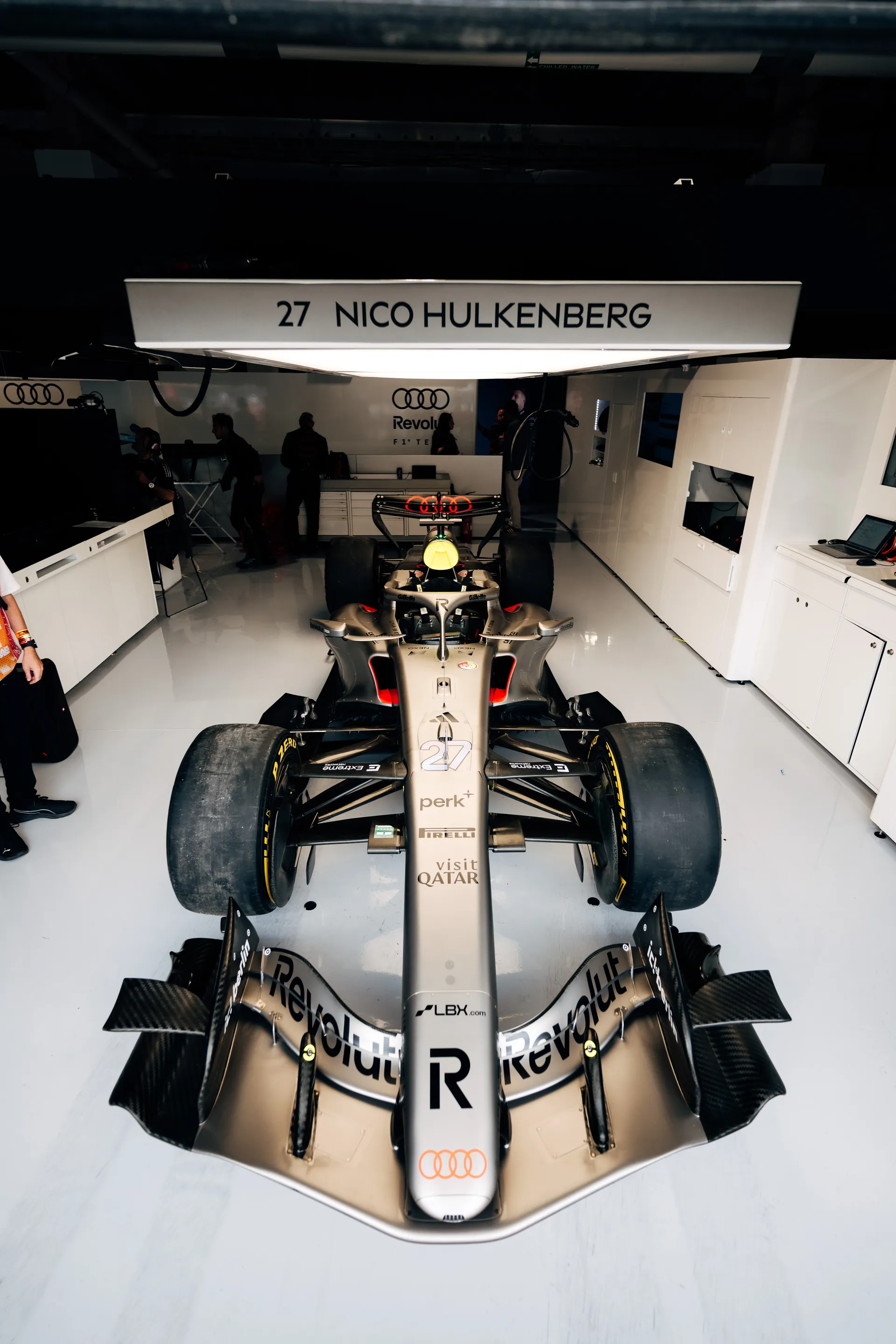 Audi Revolut F1® Team car number 27 parked inside the garage beneath a “Nico Hulkenberg” name panel, with the car centered and ready for track action.